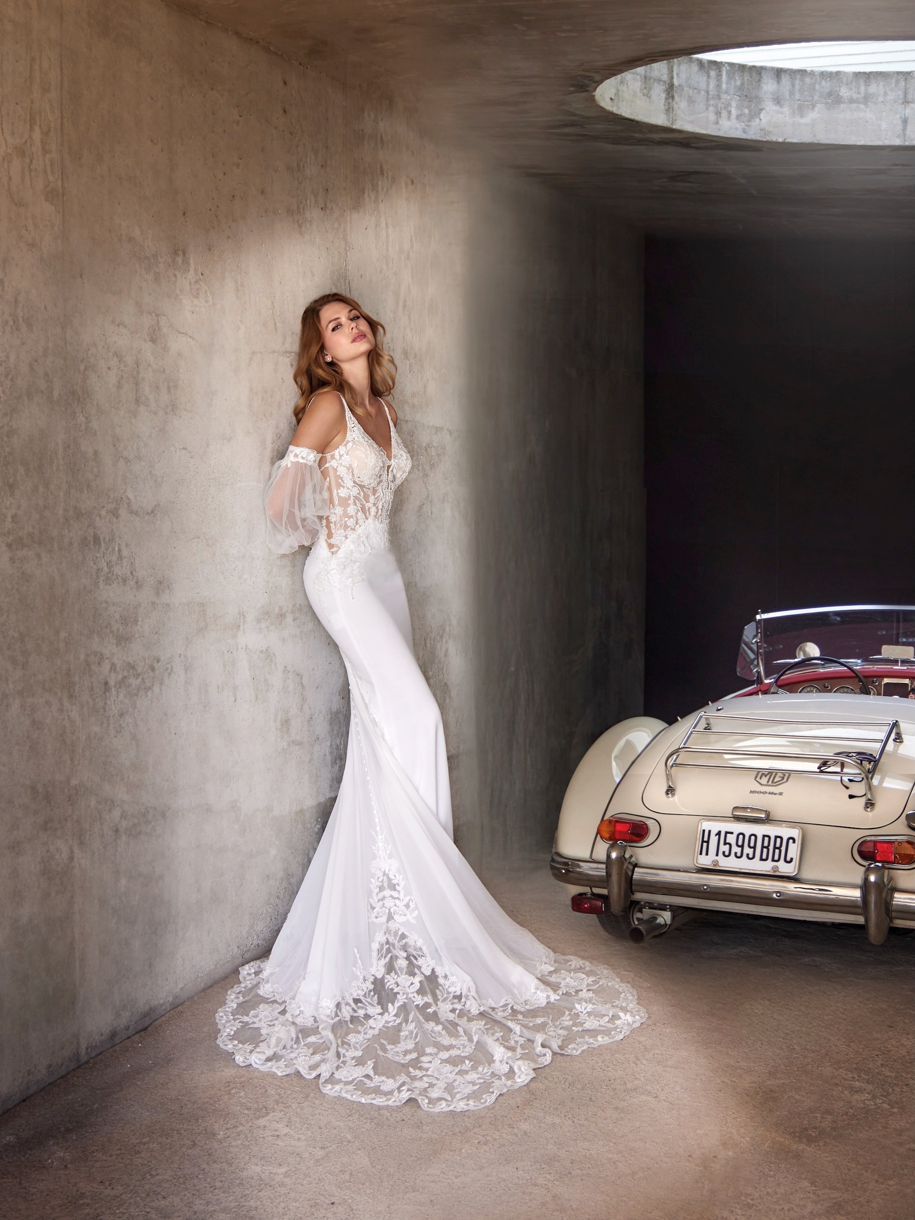 Woman in a white wedding dress standing in a modern architectural setting with a vintage car.