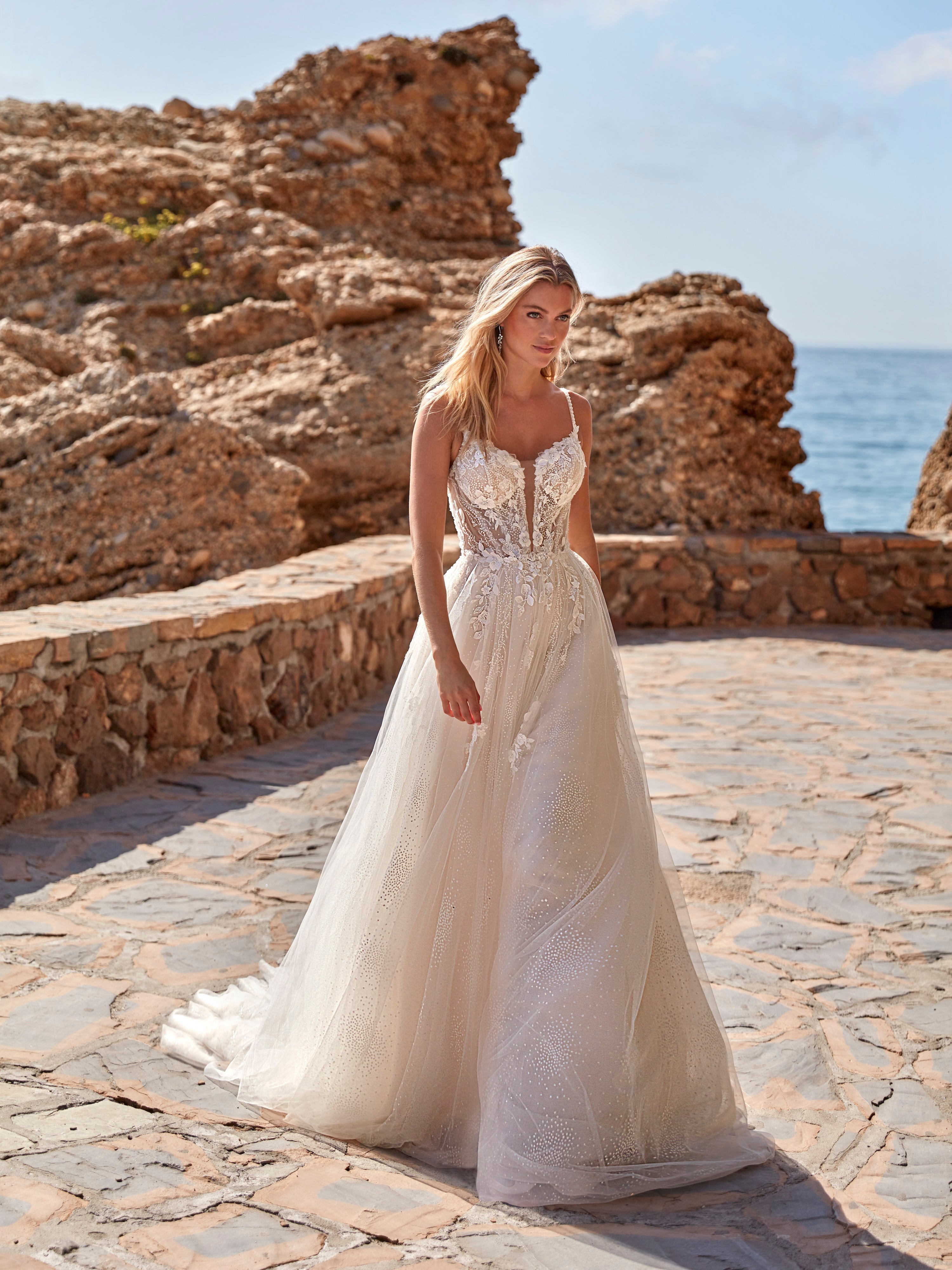 Woman in a wedding dress standing on a stone path with ocean and rocks in the background