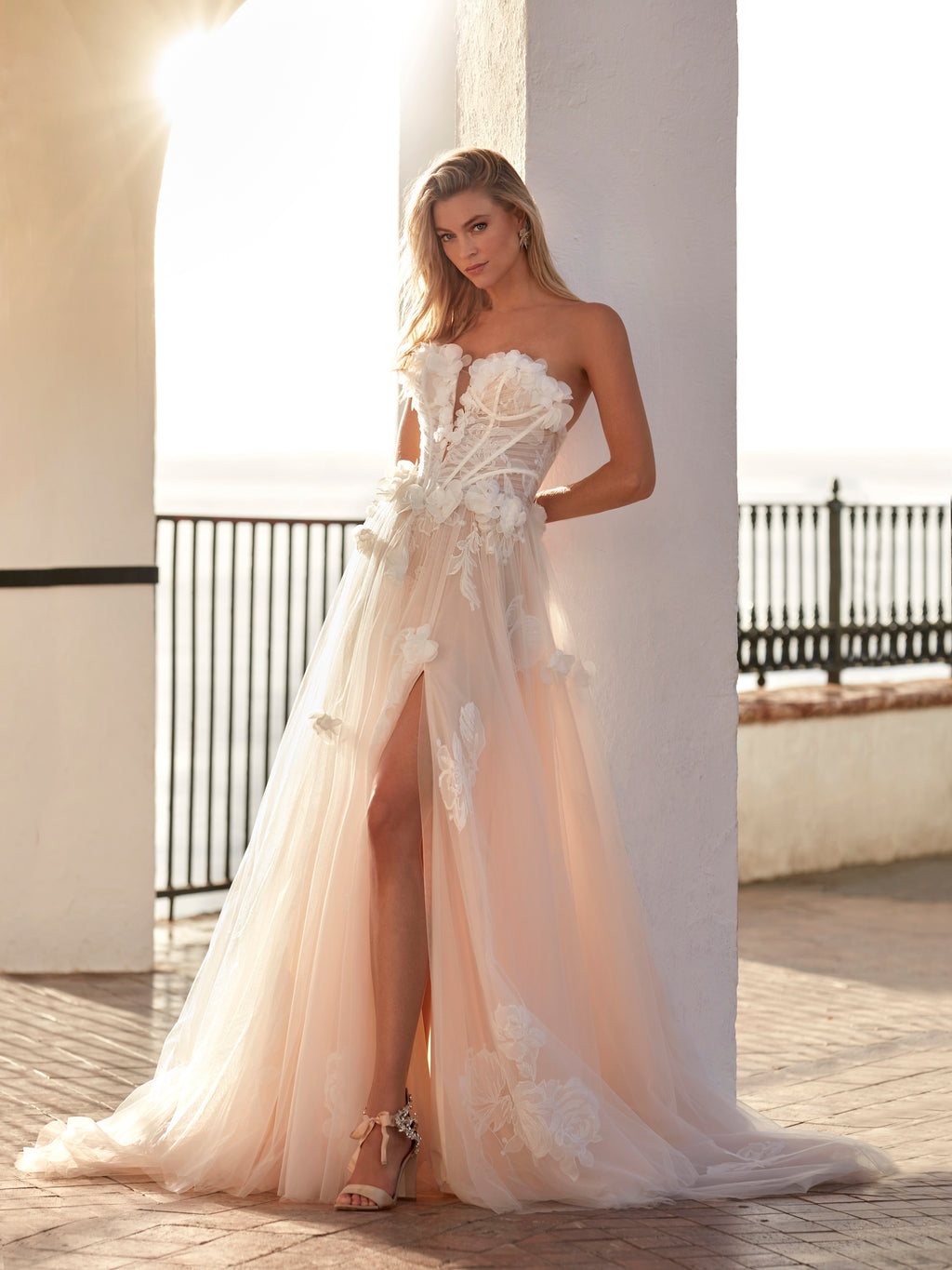 Woman in a strapless floral wedding dress with a high slit on a balcony.