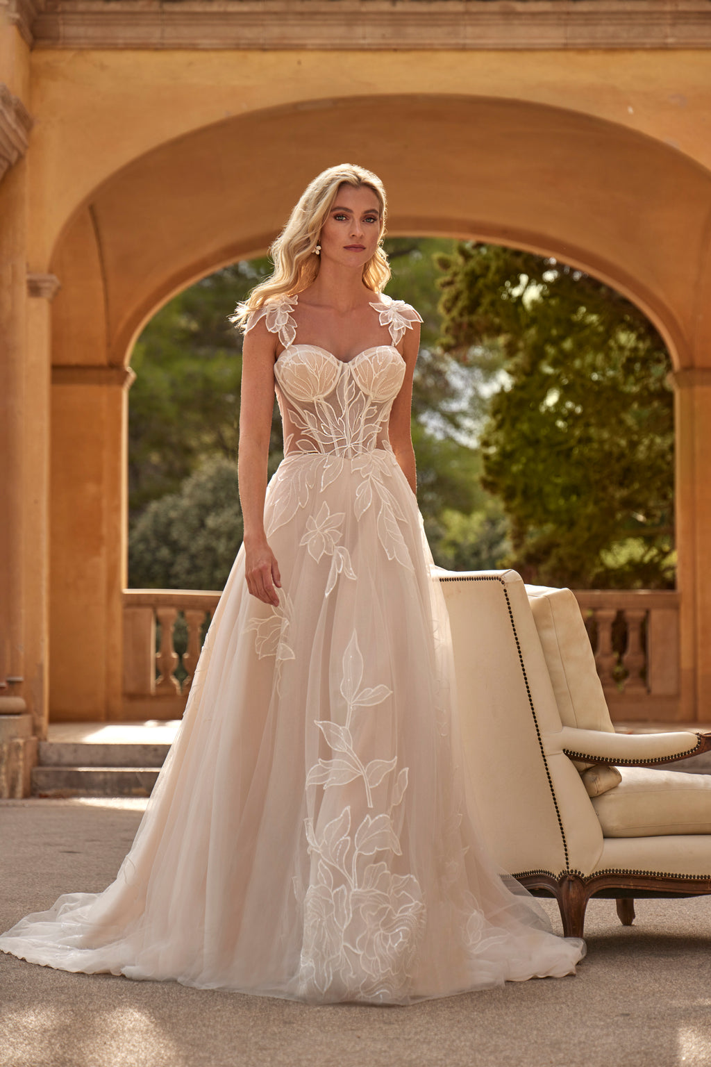 Woman in a white wedding dress standing in front of an archway with greenery.