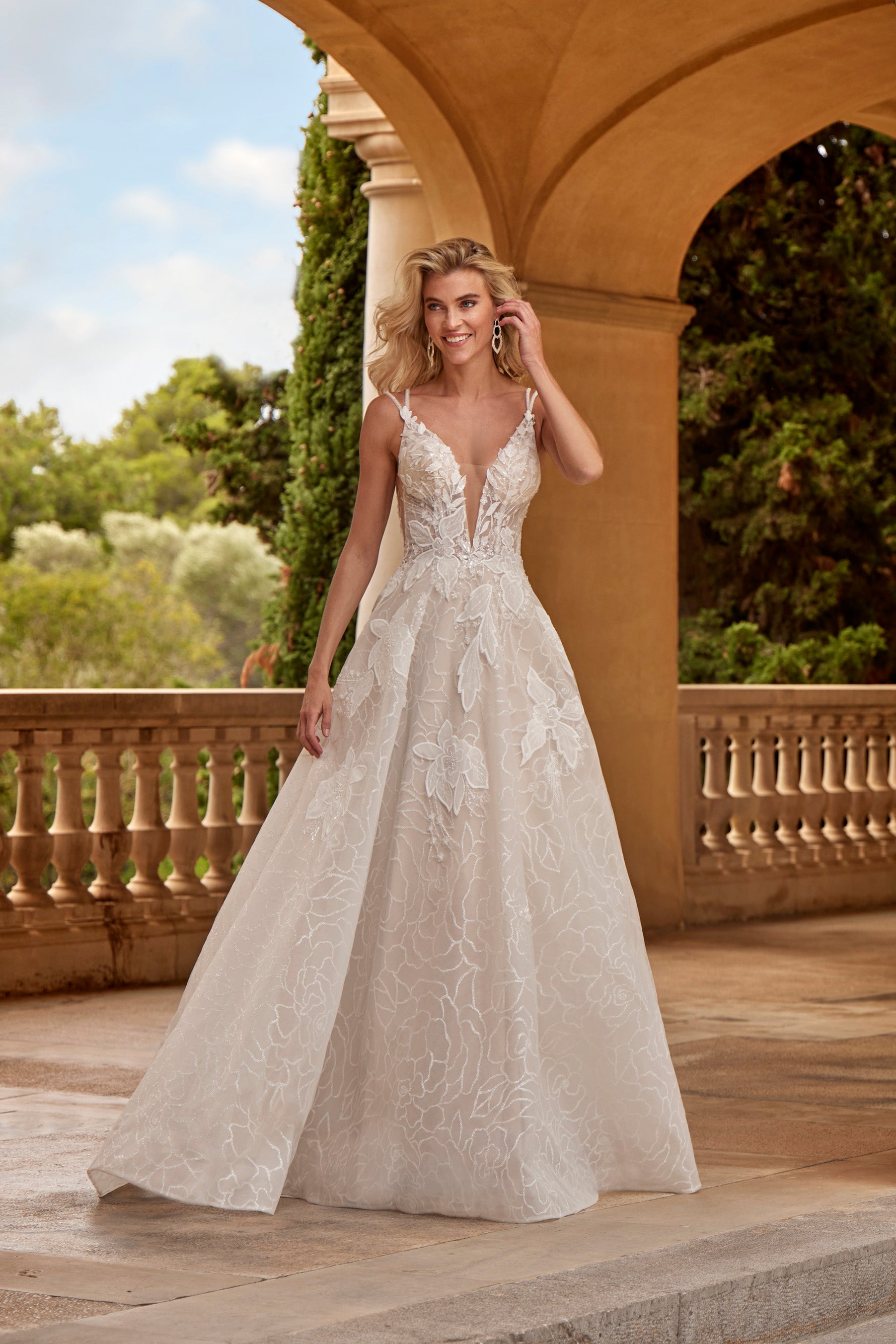 Woman in a white lace wedding dress standing outdoors with greenery in the background