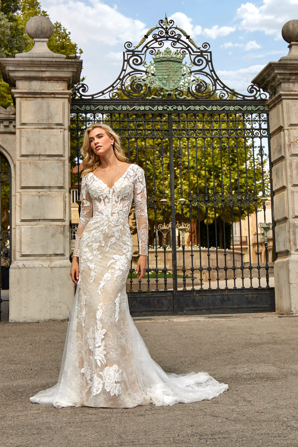 Woman in a white lace wedding dress standing in front of an ornate gate.