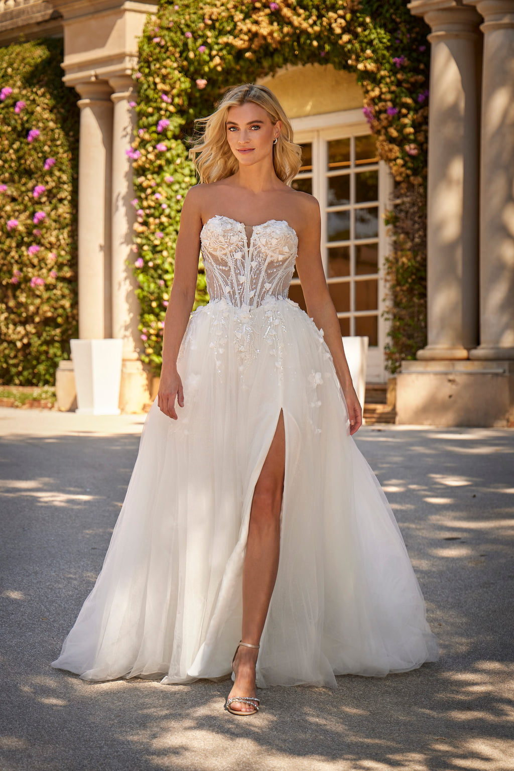 Woman in a white strapless gown with floral details standing outdoors.
