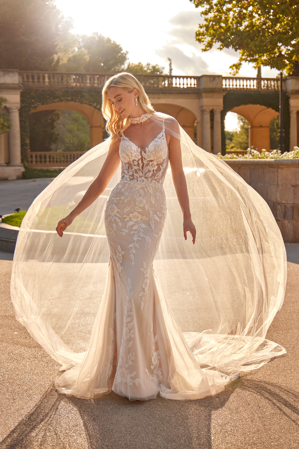 Woman in a white wedding dress with a long train standing outdoors.