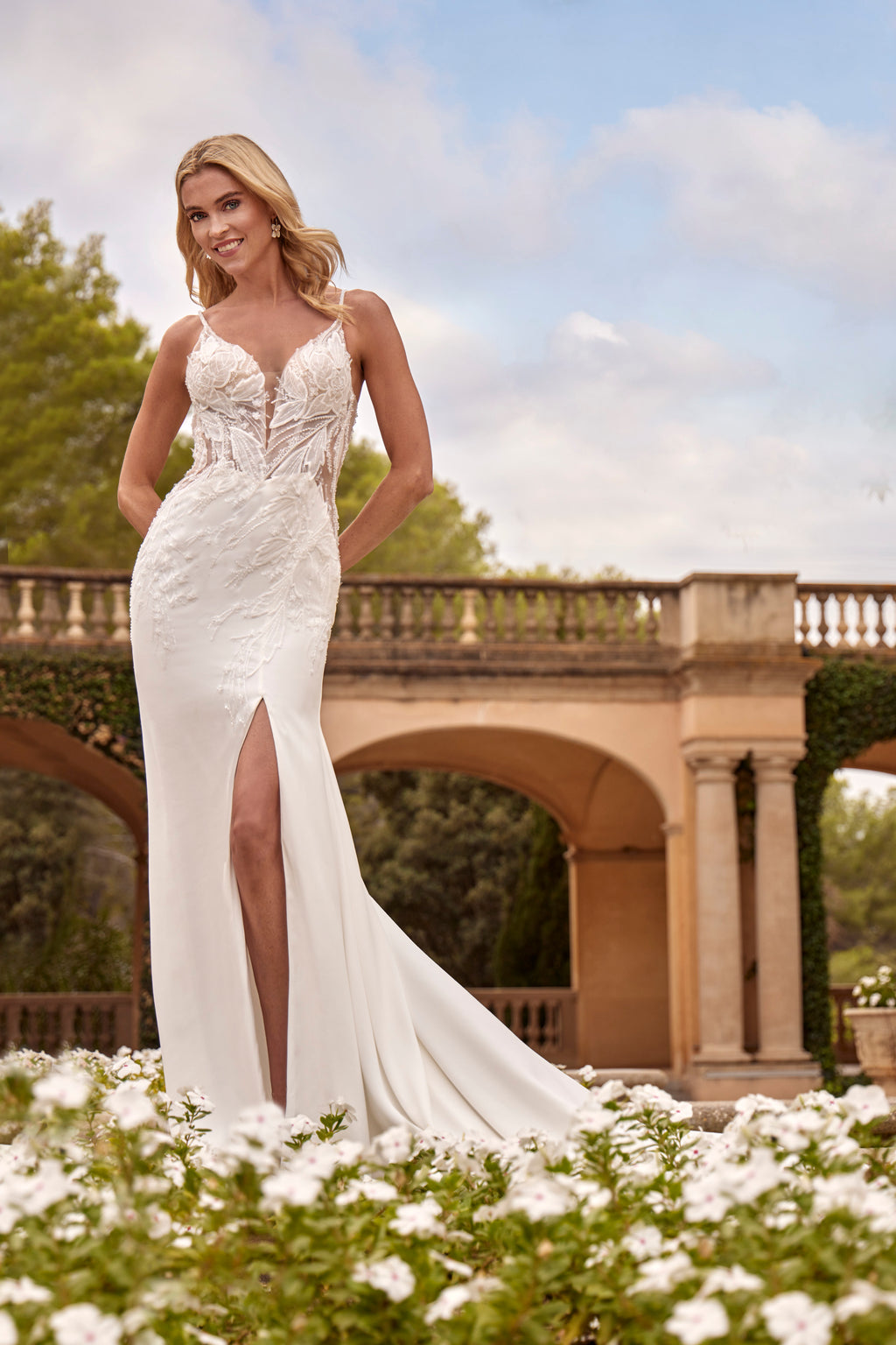 Woman in a white wedding dress standing outdoors with greenery and a bridge in the background
