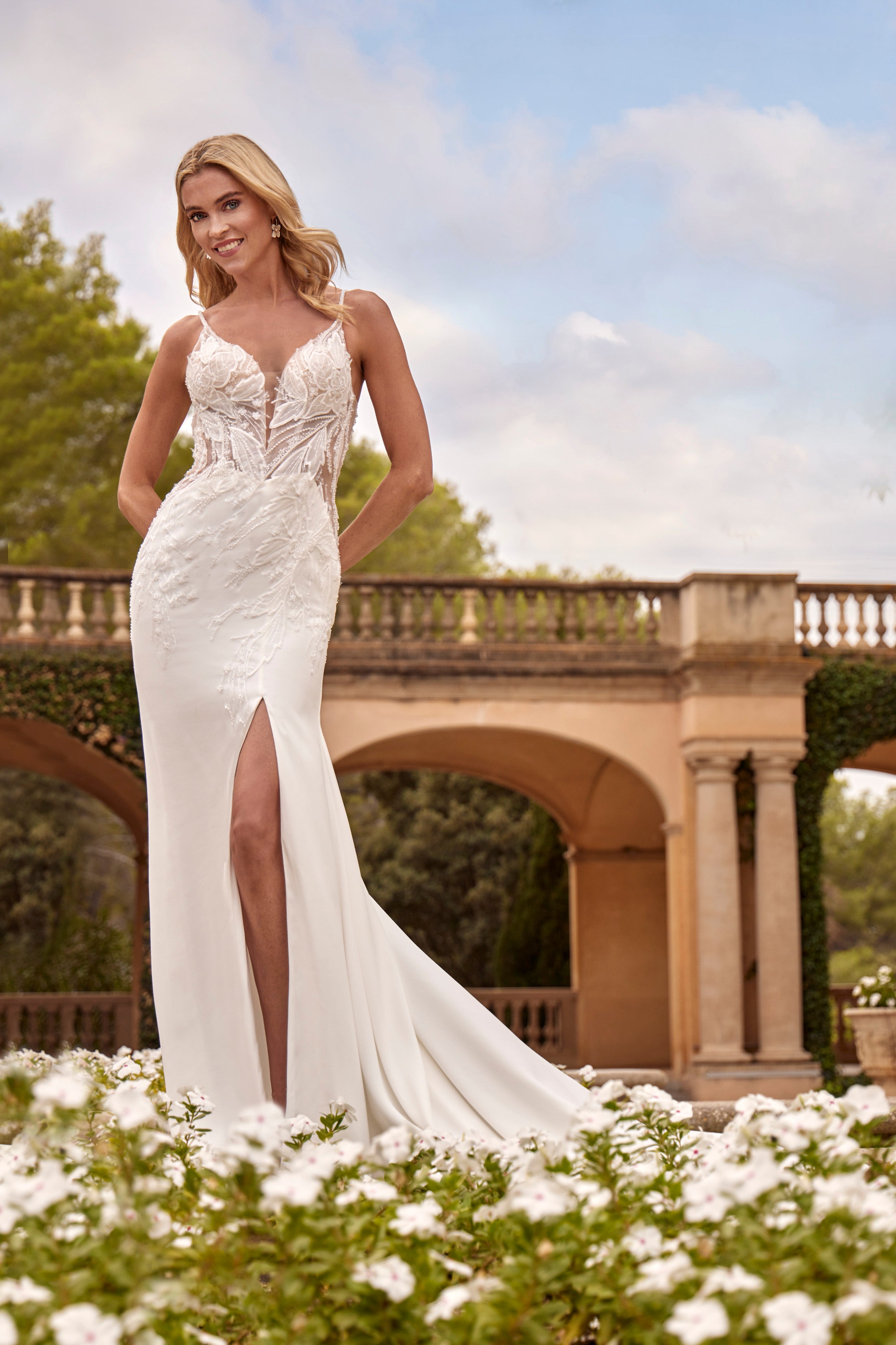 Woman in a white wedding dress standing outdoors with greenery and a bridge in the background