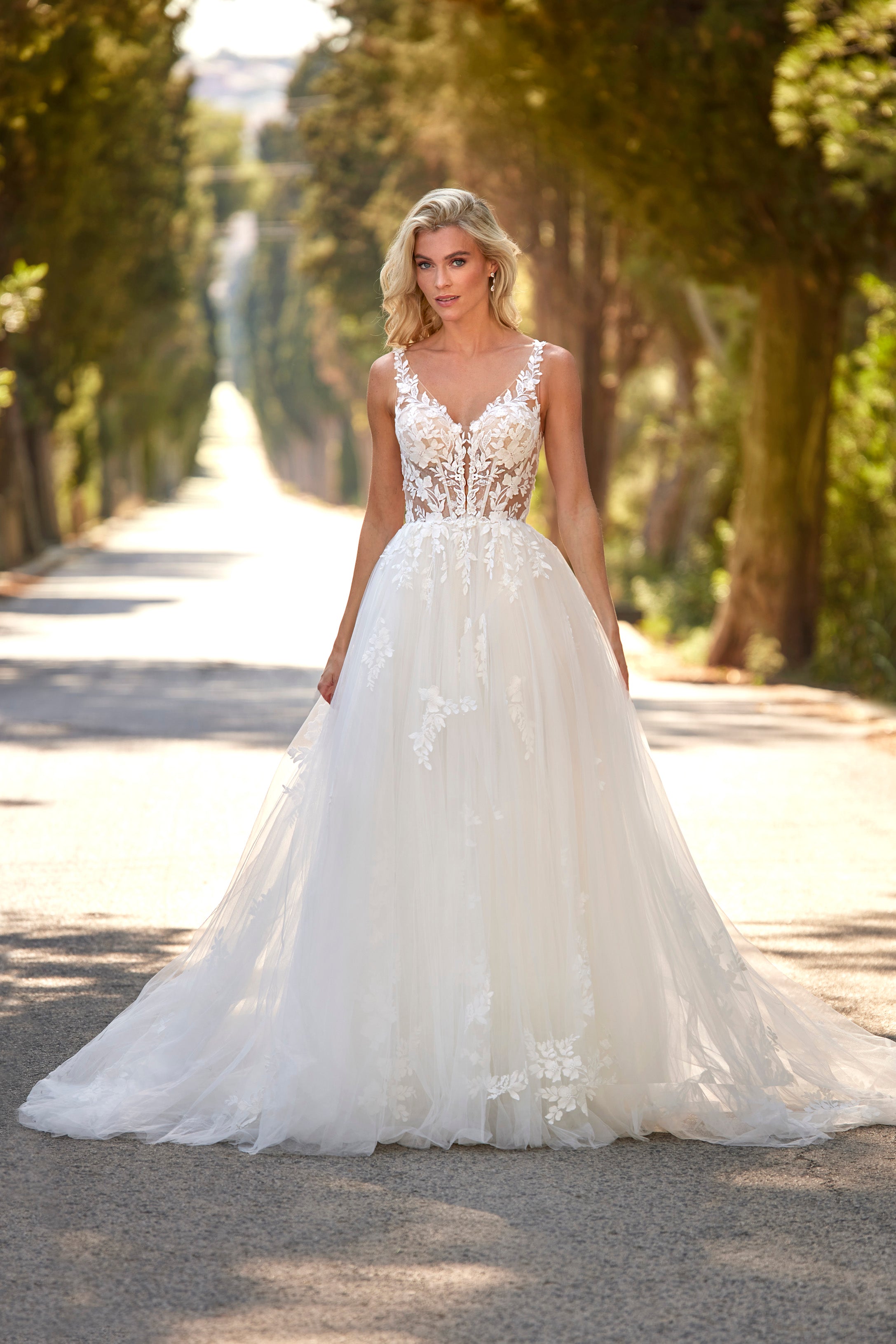Woman in a white wedding dress standing on a tree-lined path
