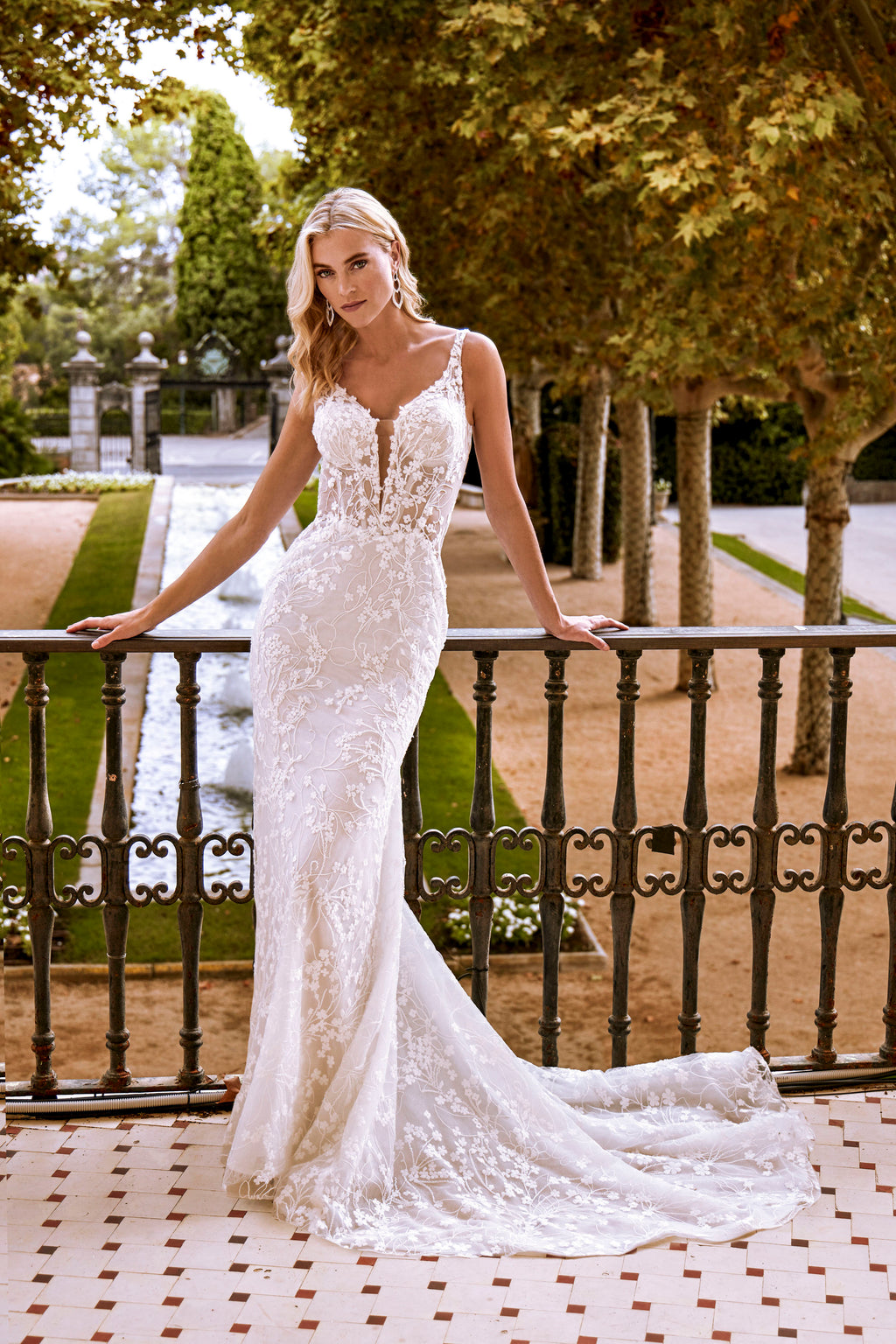 Woman in a white wedding dress standing on a balcony with trees and water in the background