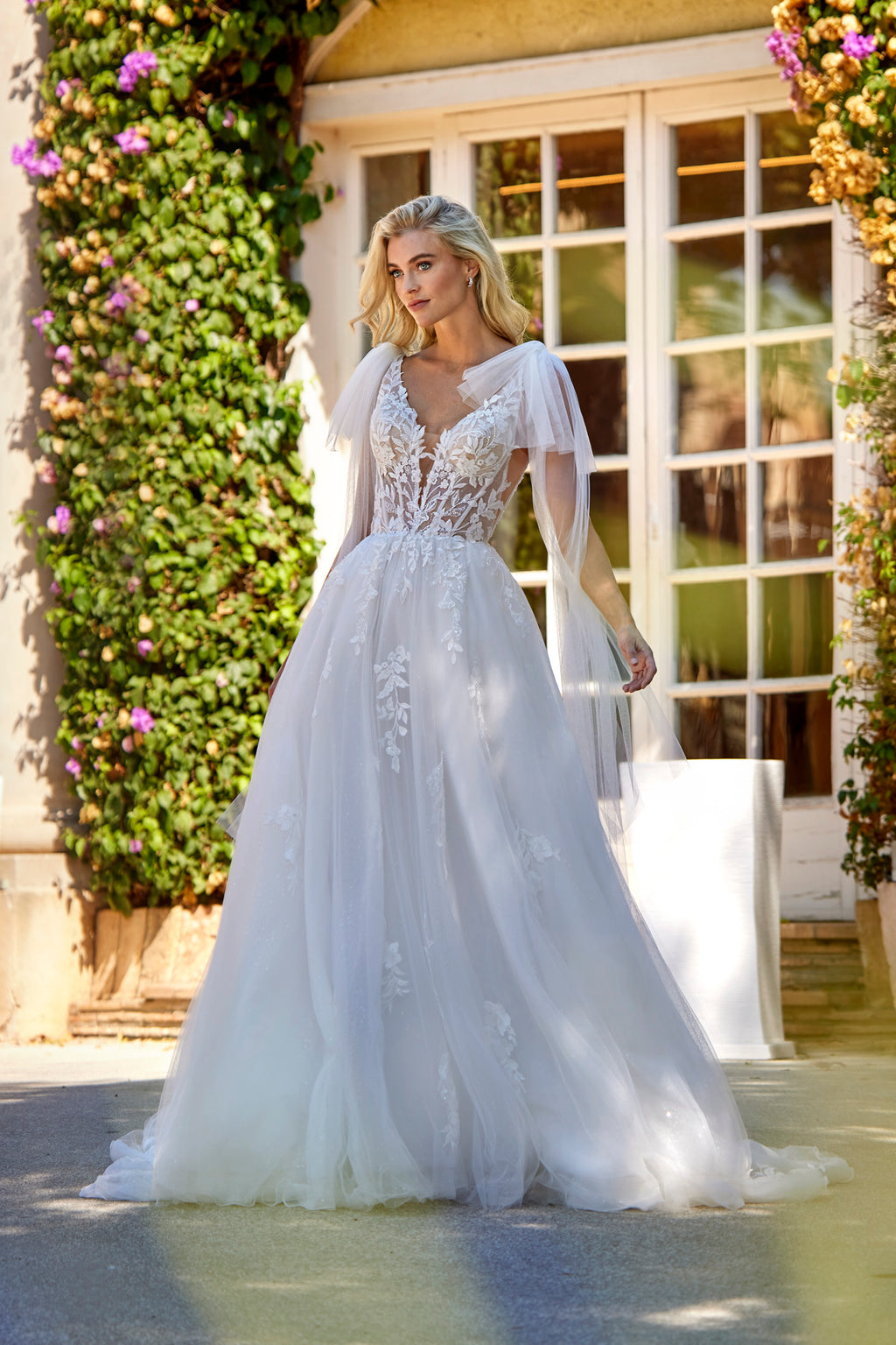 Woman in a white wedding dress standing in front of a building with floral decorations.