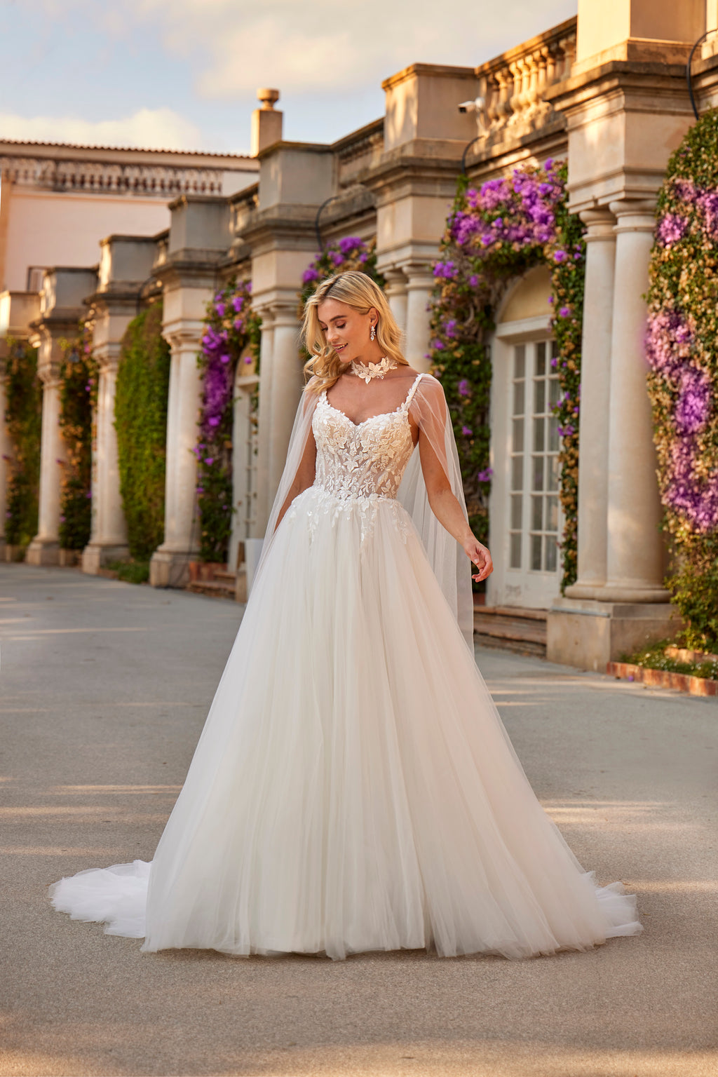 Woman in a white wedding dress standing in front of classical architecture with floral decorations.
