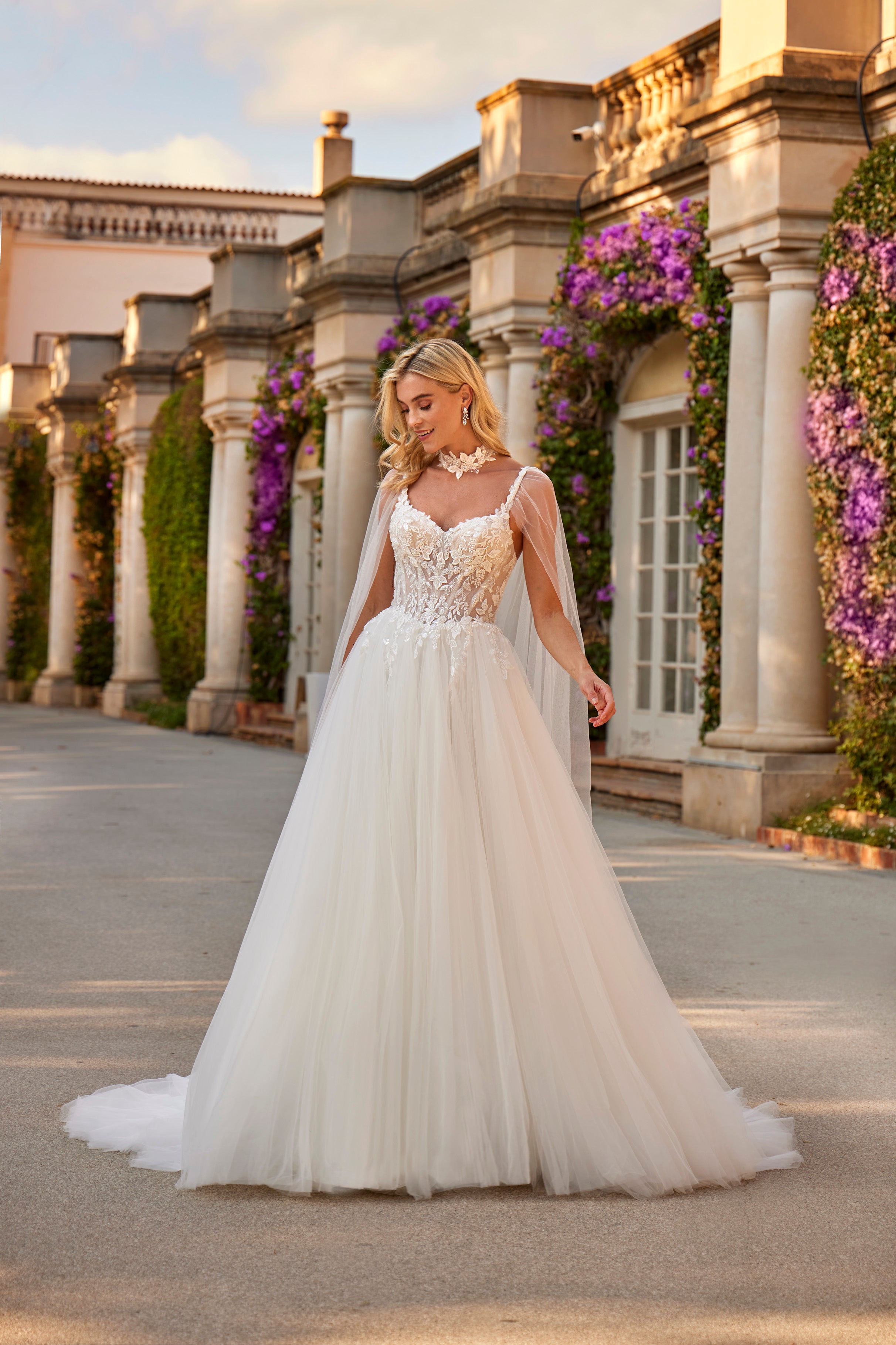 Woman in a white wedding dress standing in front of classical architecture with floral decorations.