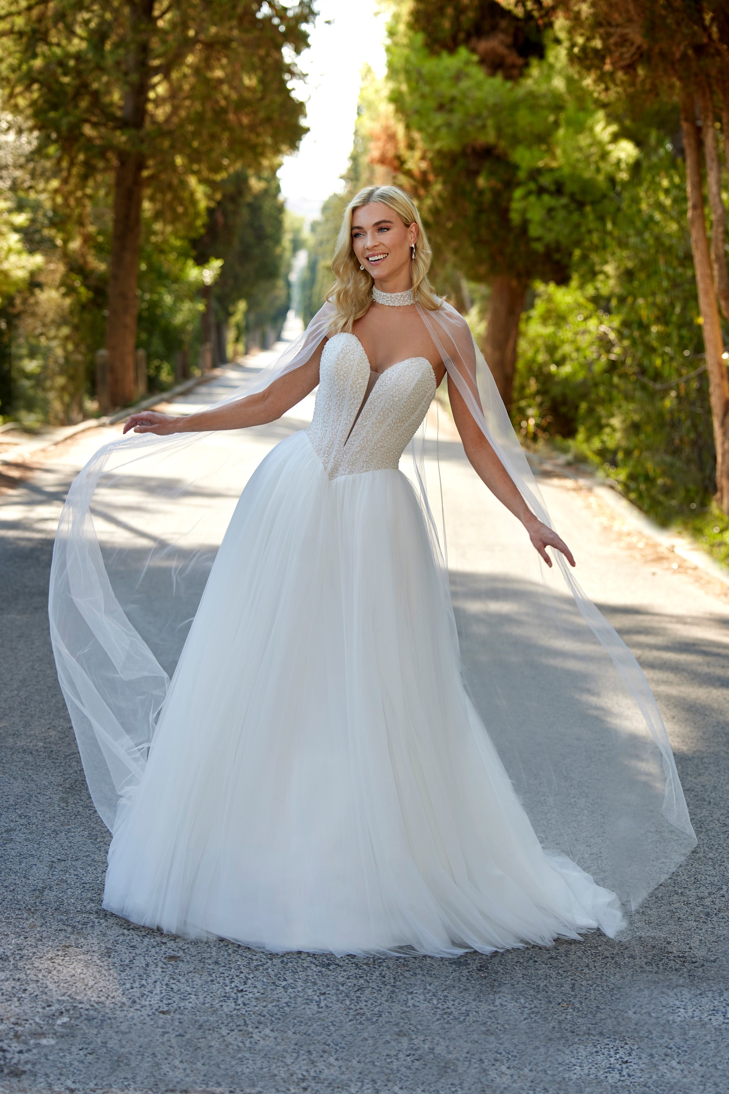 Woman in a white wedding dress standing on a path with trees in the background