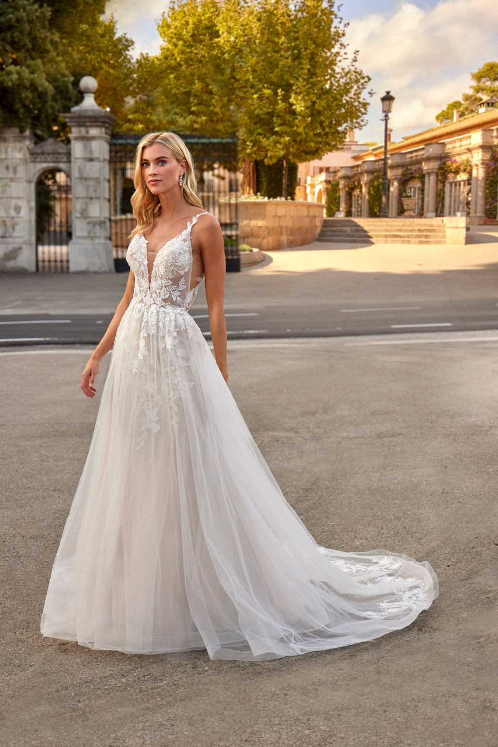 Woman in a white wedding dress standing on a street with trees and buildings in the background