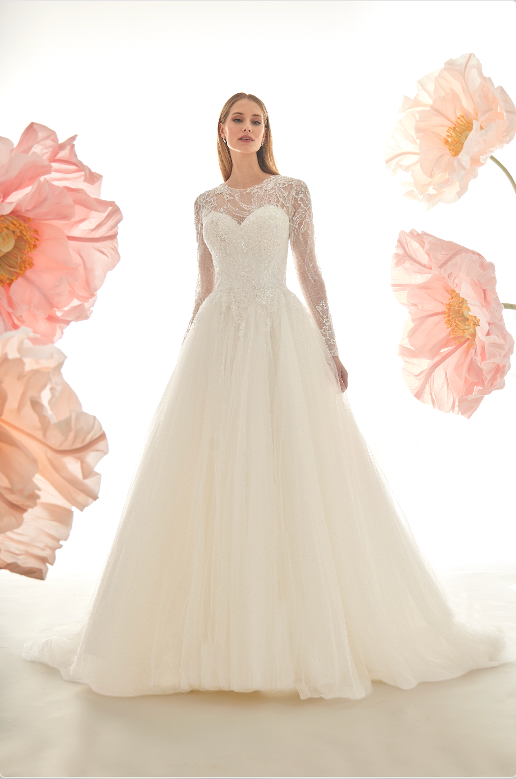 White wedding dress with long sleeves against a white background with pink flowers.