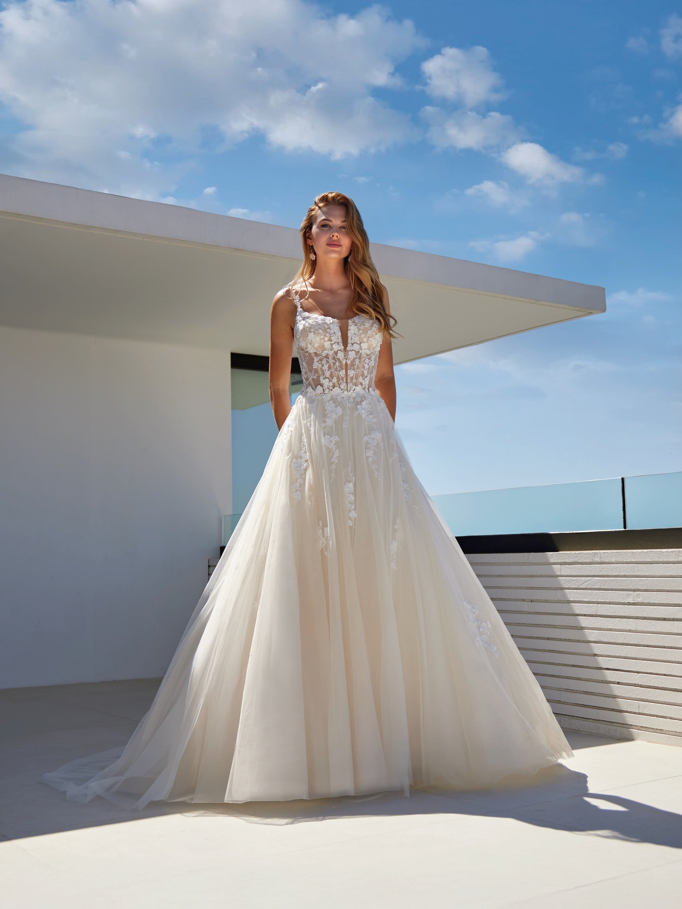Woman in a white wedding dress standing on a rooftop with a clear blue sky.