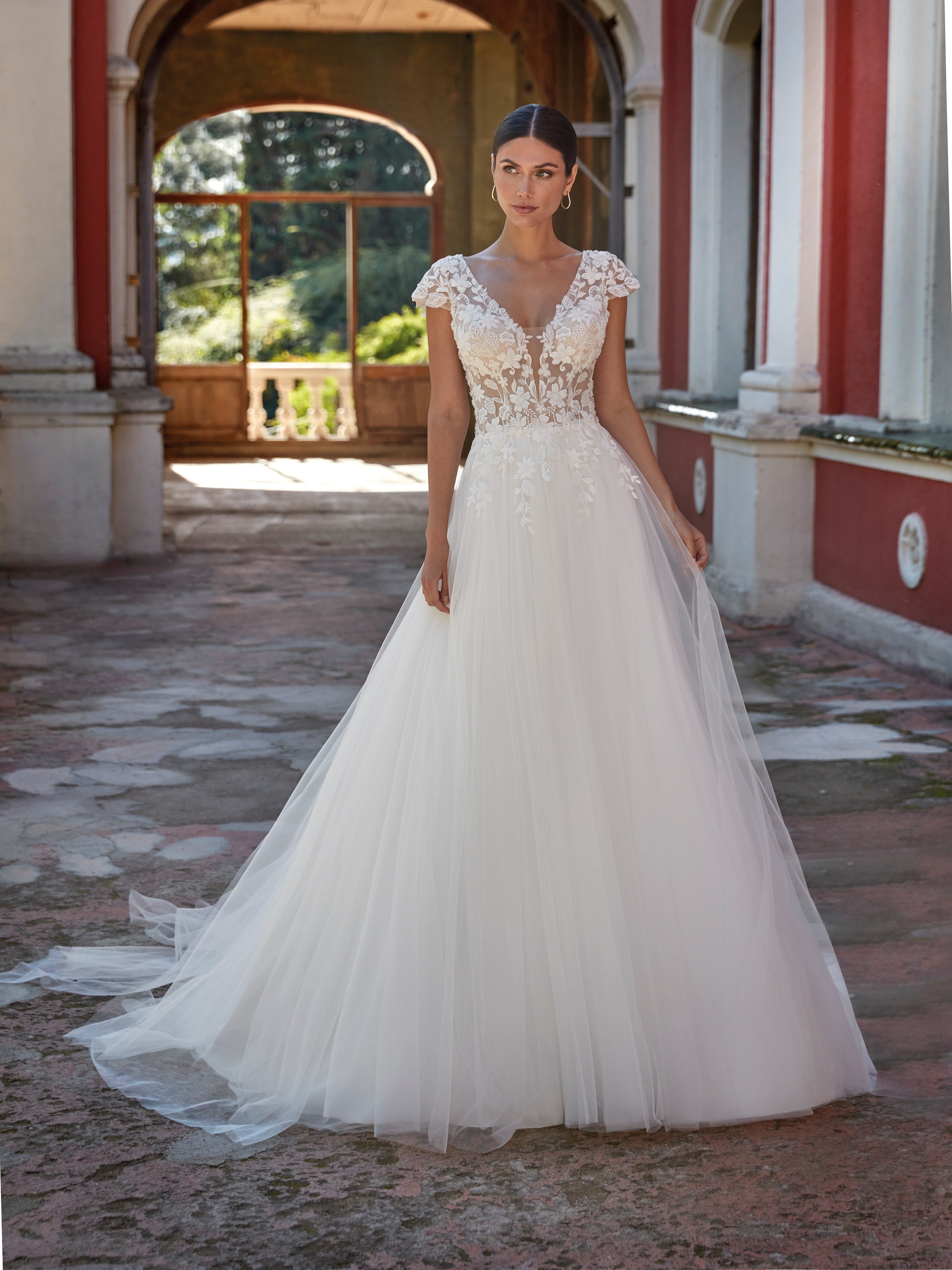 Woman in a white wedding dress standing in an outdoor setting with classical architecture.