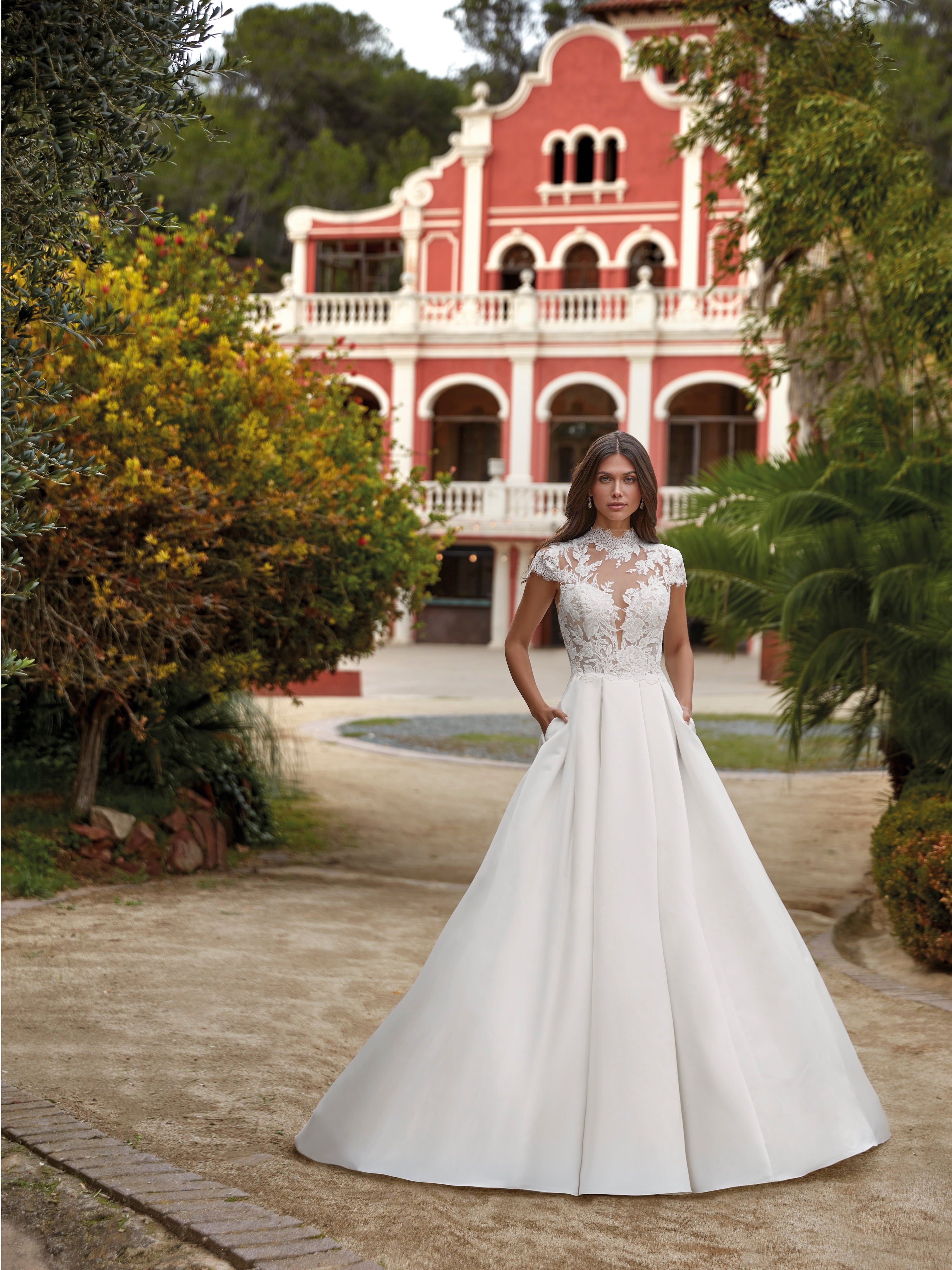 Woman in a white wedding dress standing in front of a red and white building with greenery.
