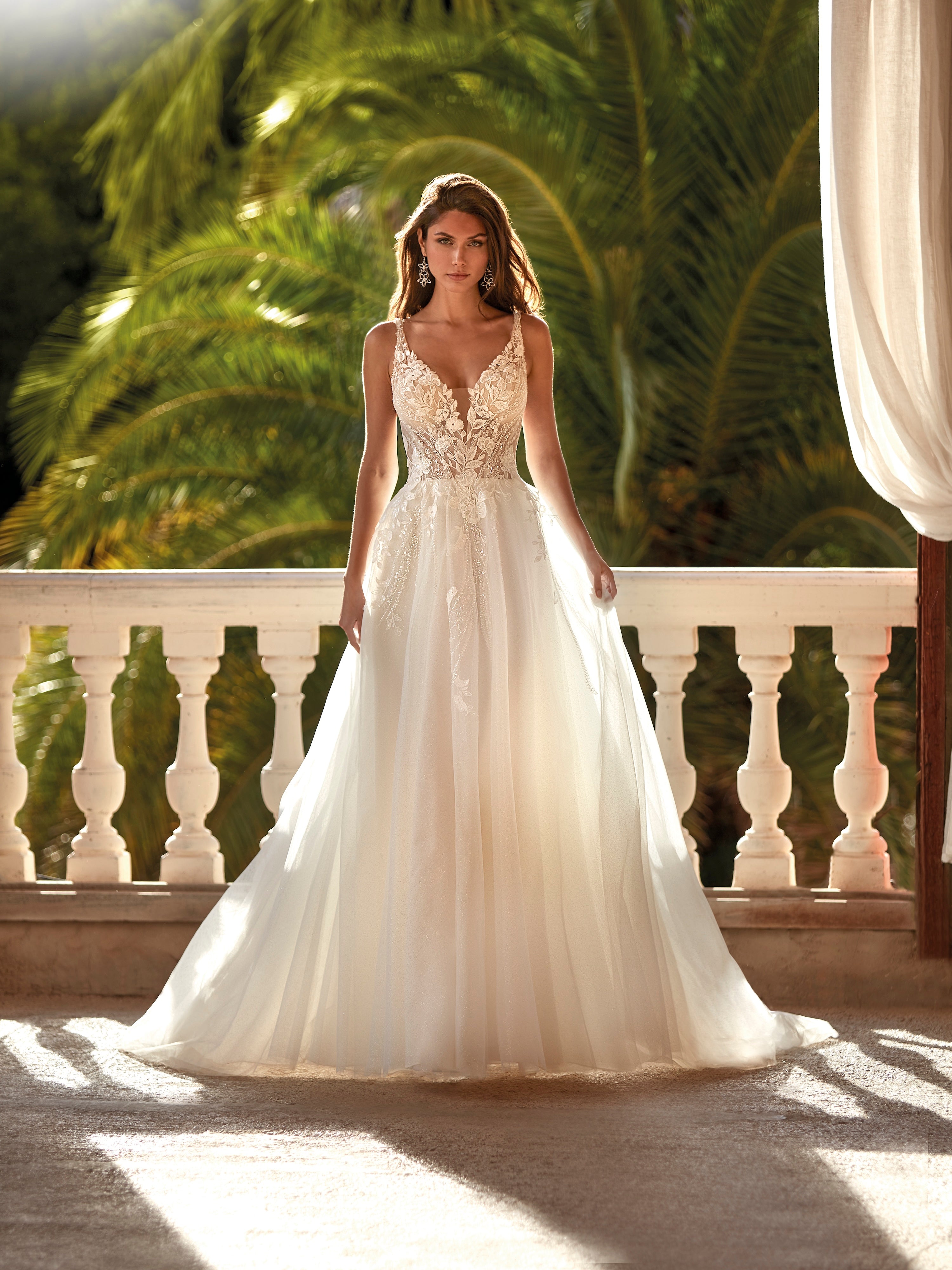 Woman in a white wedding dress standing on a balcony with greenery in the background
