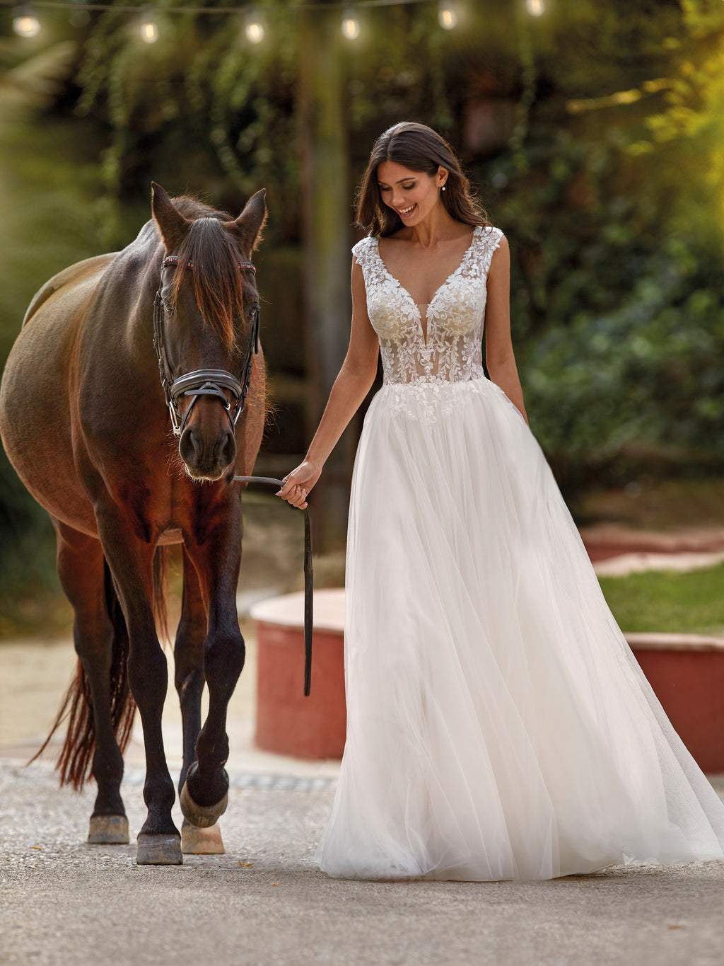 Woman in a white wedding dress walking a horse in a garden setting