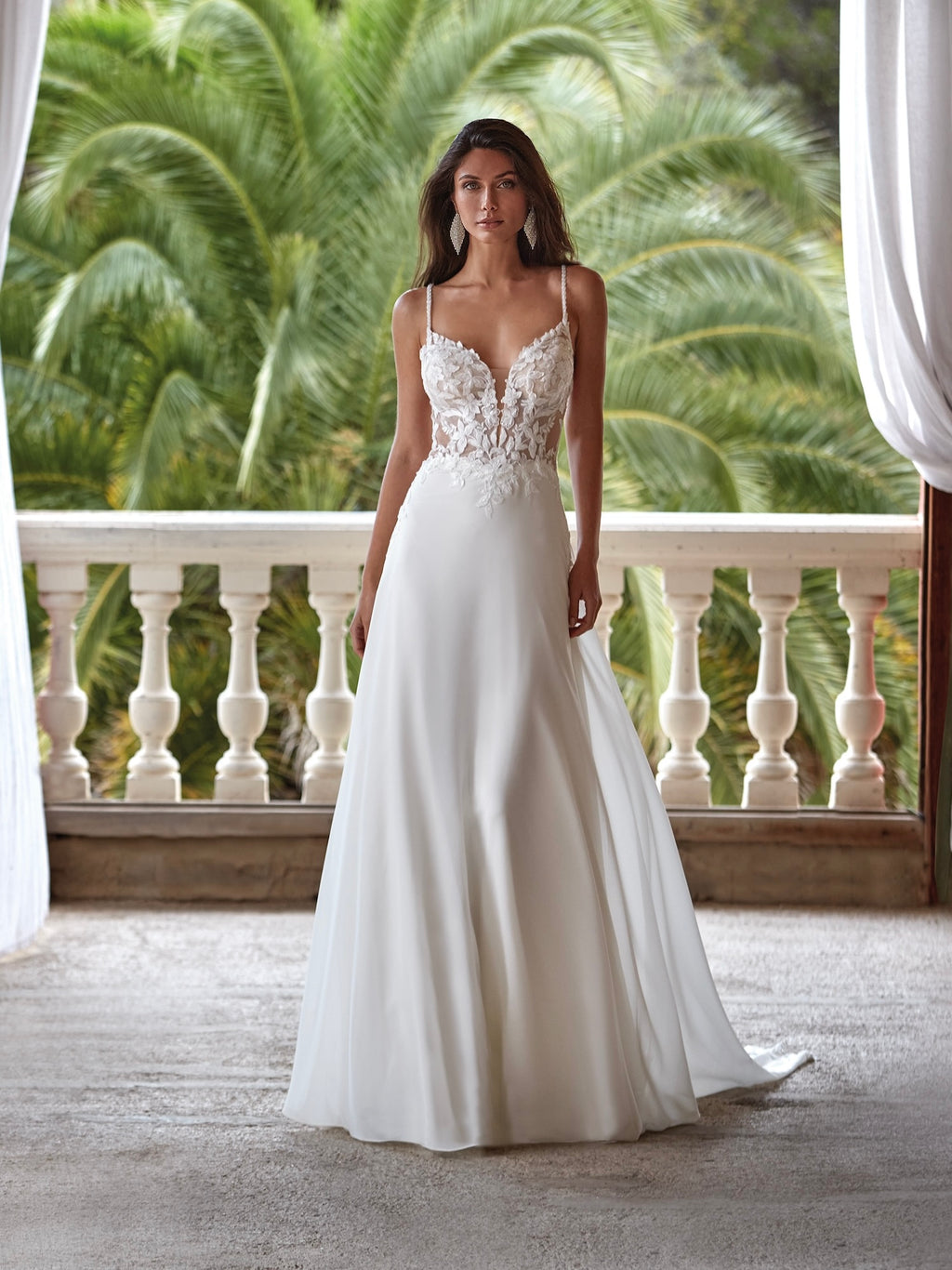 Woman in a white wedding dress standing on a balcony with palm trees in the background