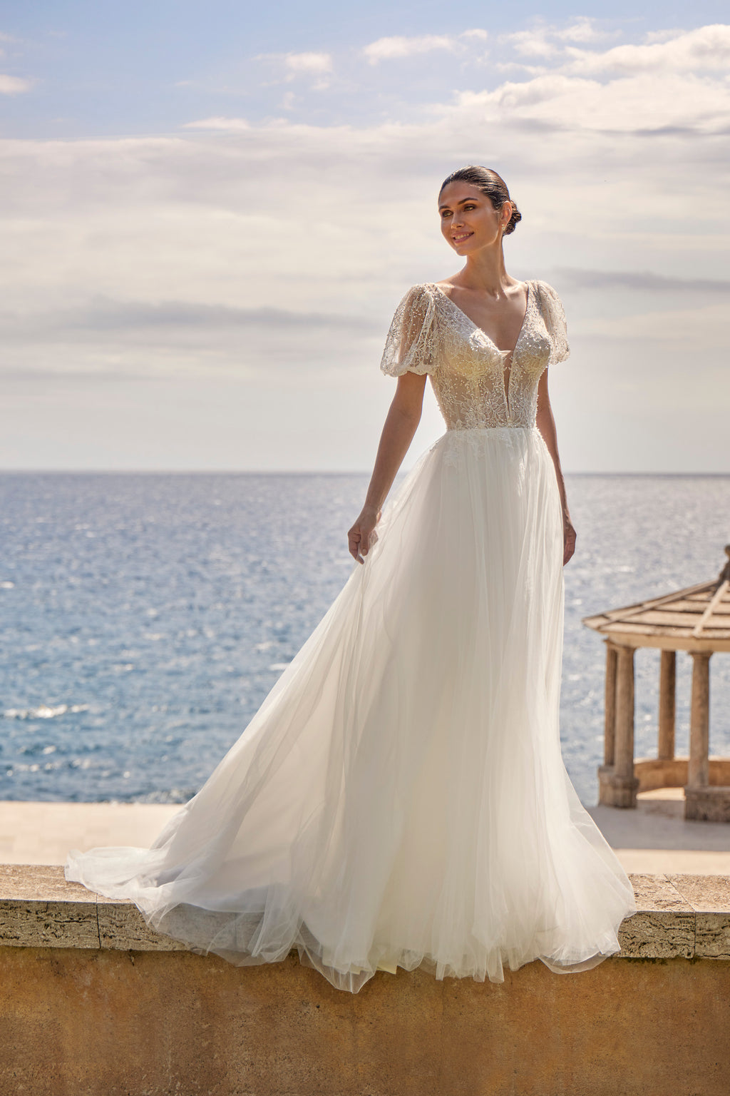 Woman in a white wedding dress standing by the ocean with a scenic background