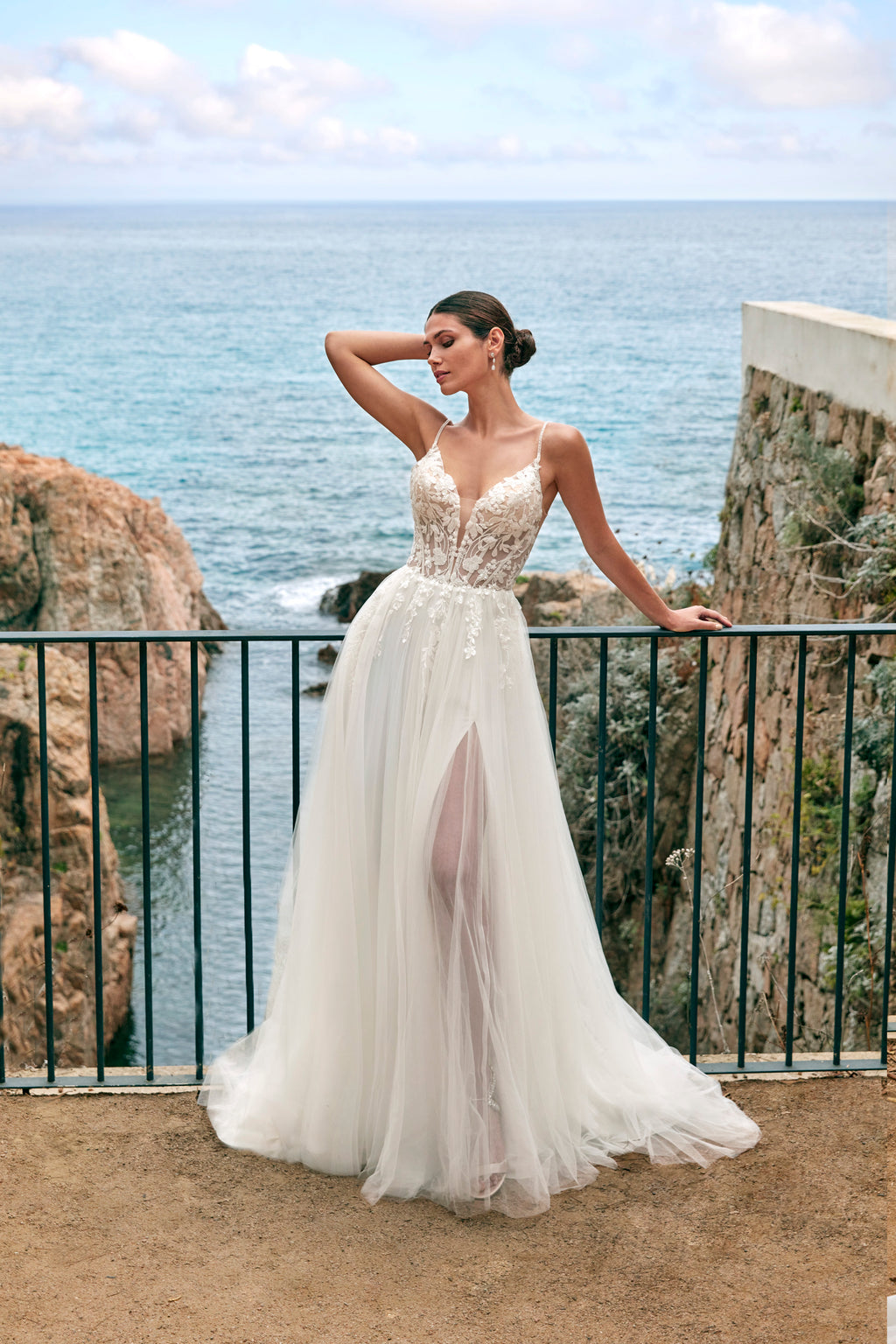 Woman in a white wedding dress standing on a cliff overlooking the ocean.