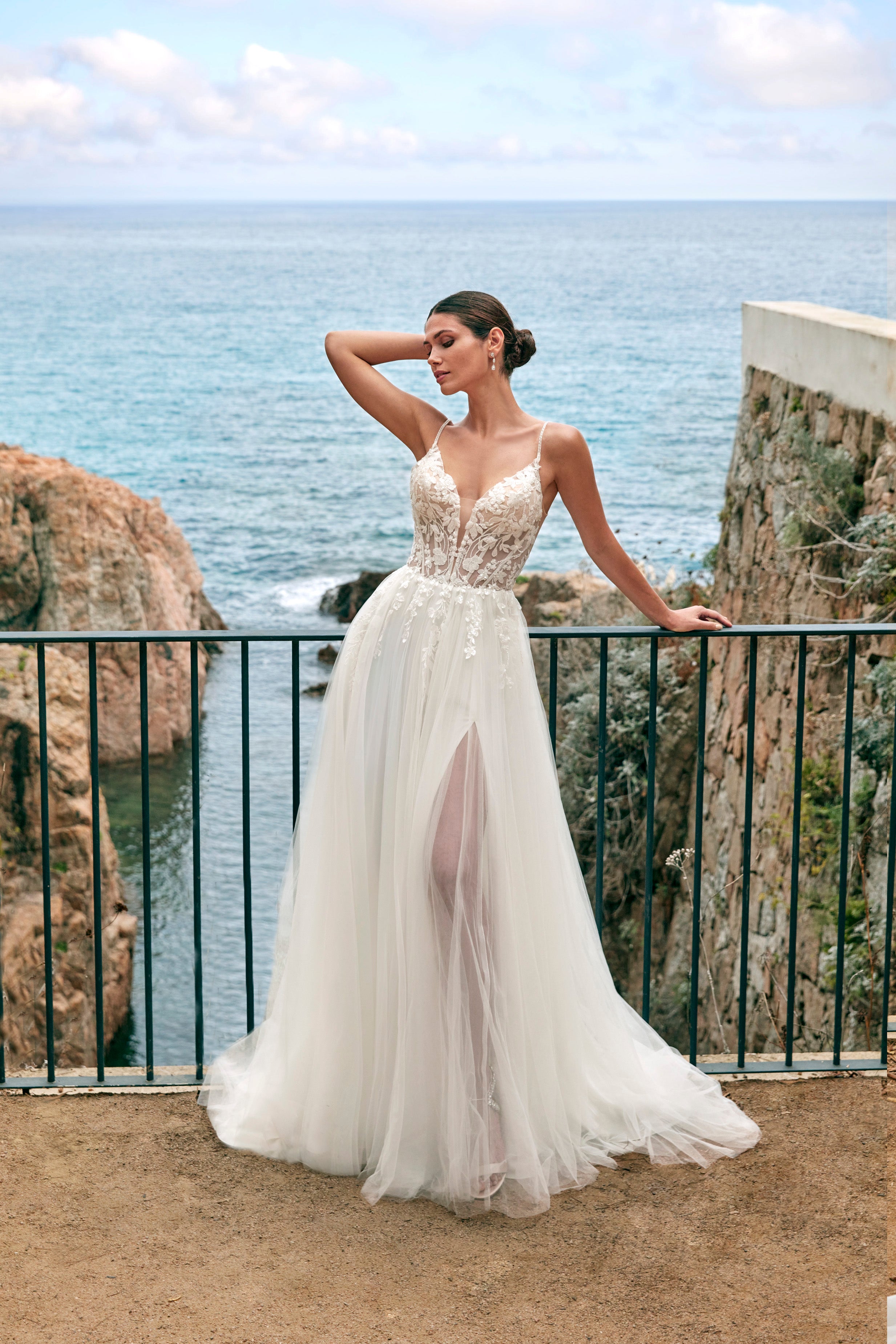 Woman in a white wedding dress standing on a cliff overlooking the ocean.