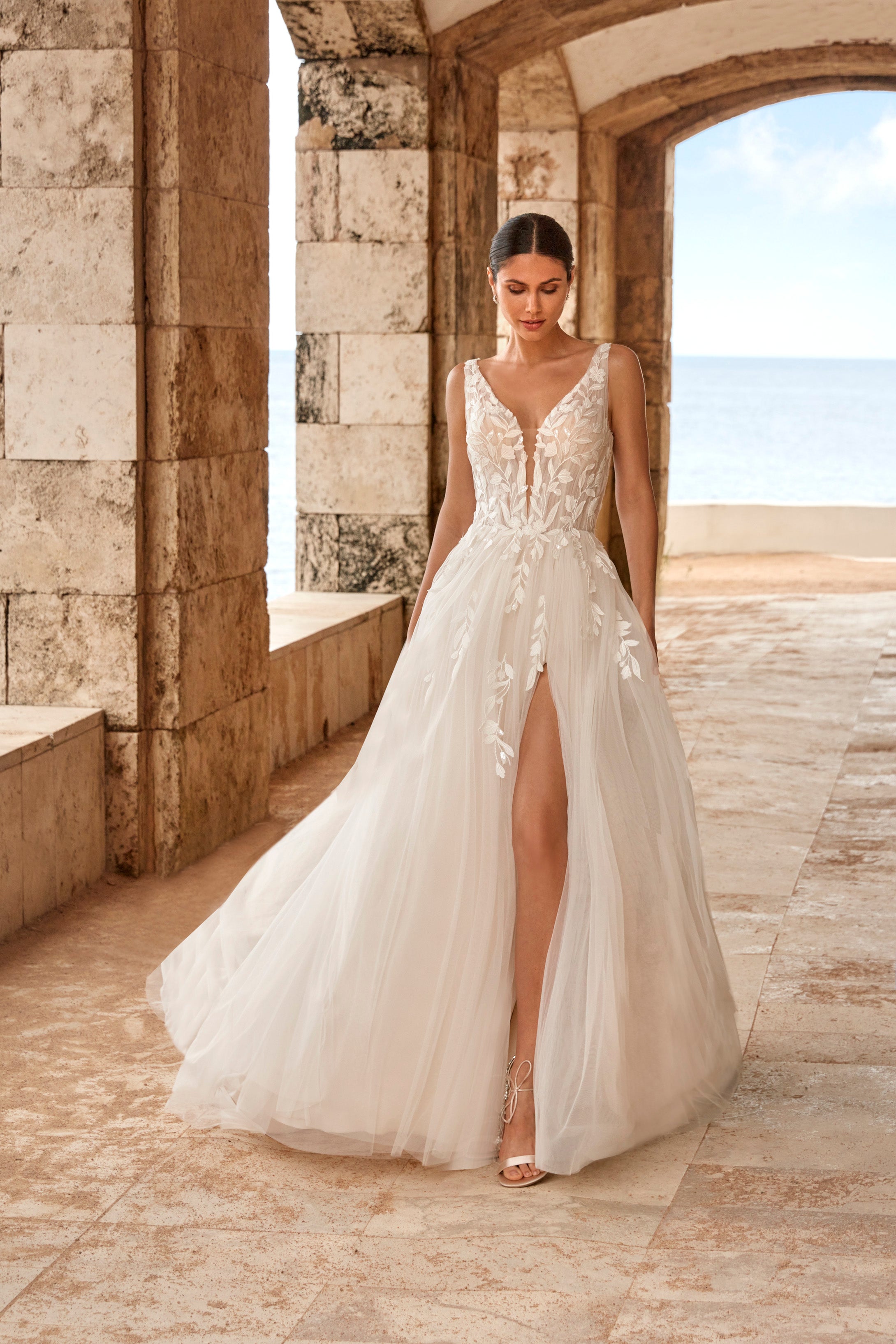 Woman in a white wedding dress standing in a stone archway with a scenic background.