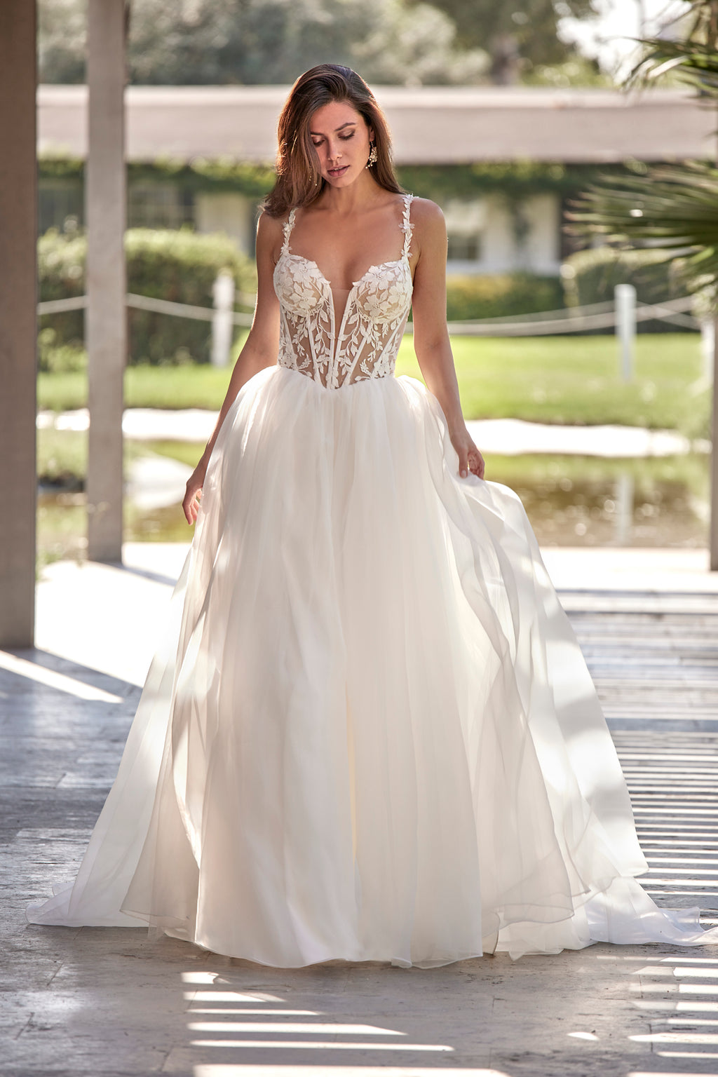 Woman in a white wedding dress standing outdoors with greenery in the background
