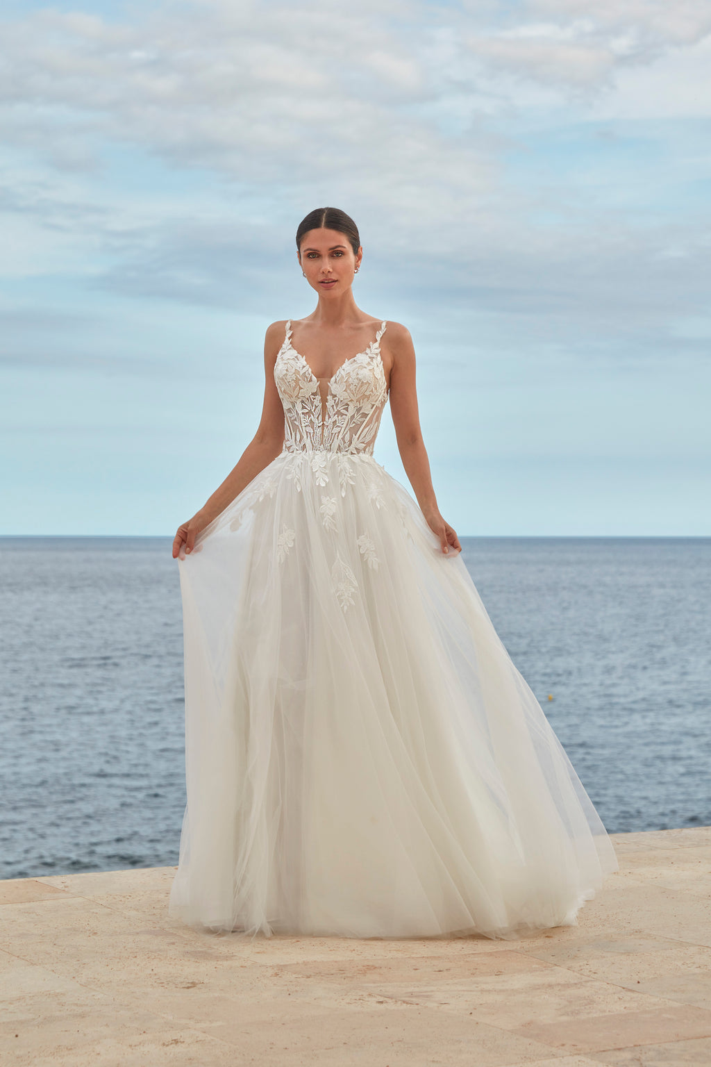 Woman in a white wedding dress standing on a beach with ocean and sky in the background