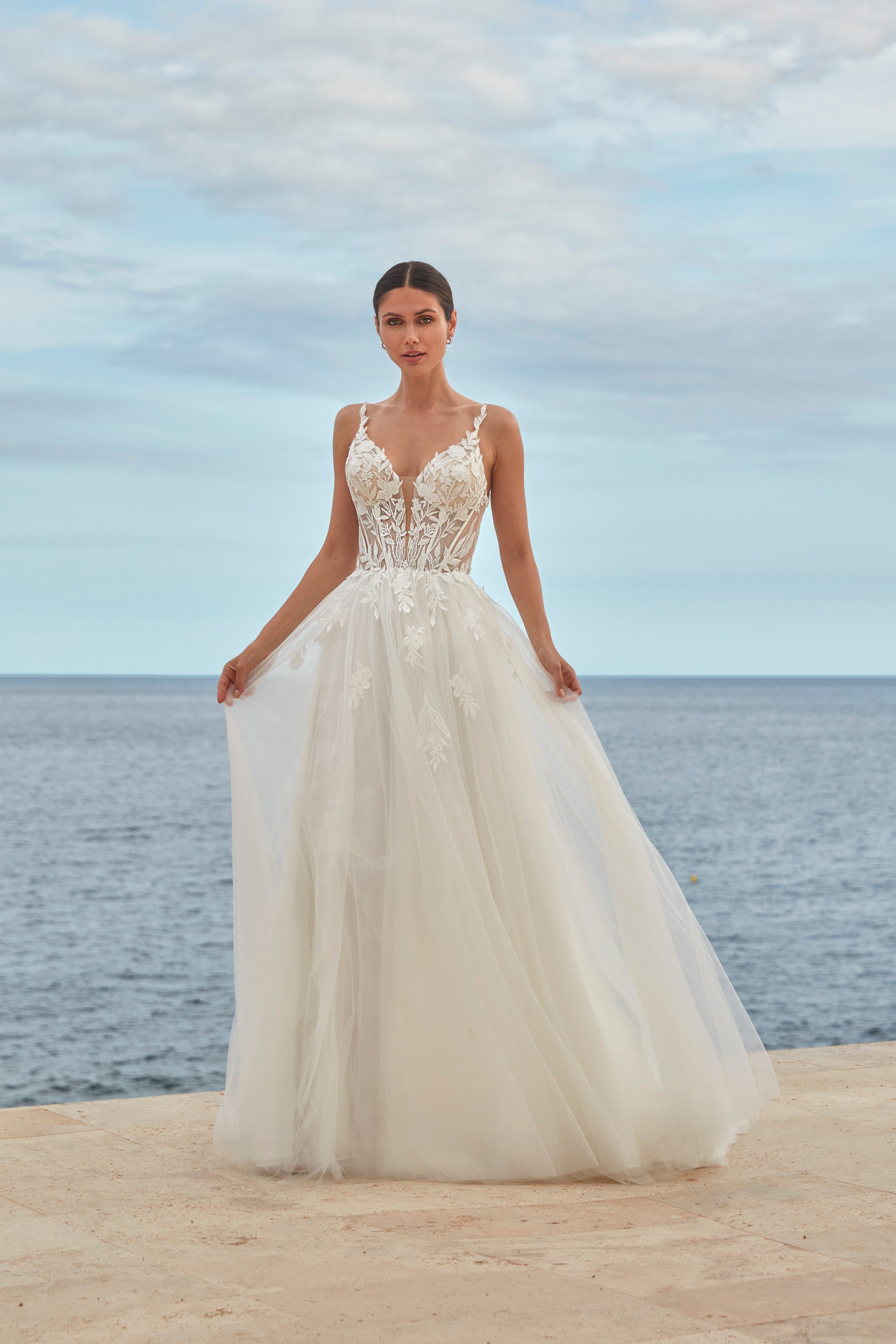 Woman in a white wedding dress standing on a beach with ocean and sky in the background