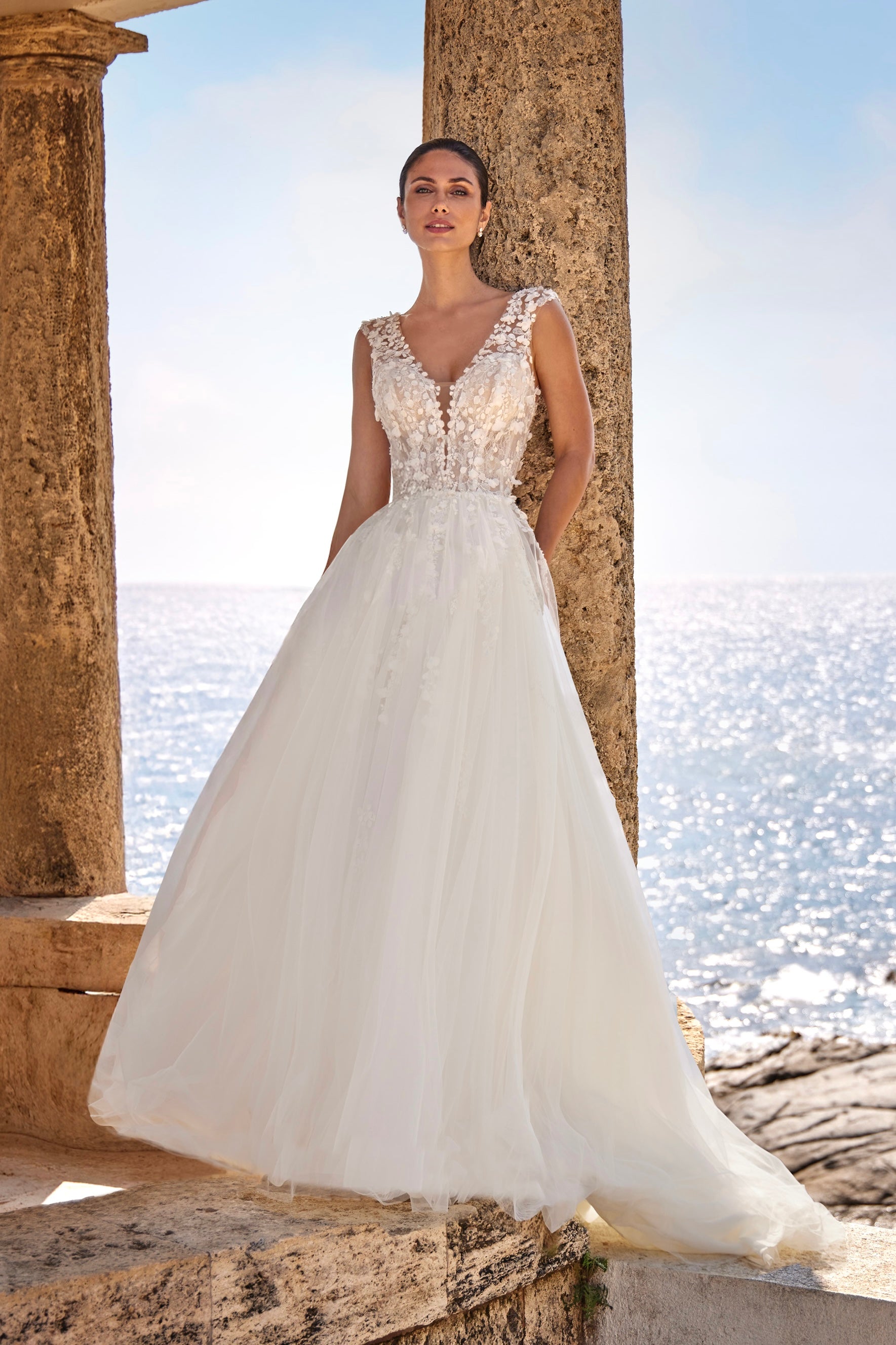 Woman in a white wedding dress standing by stone columns with water in the background