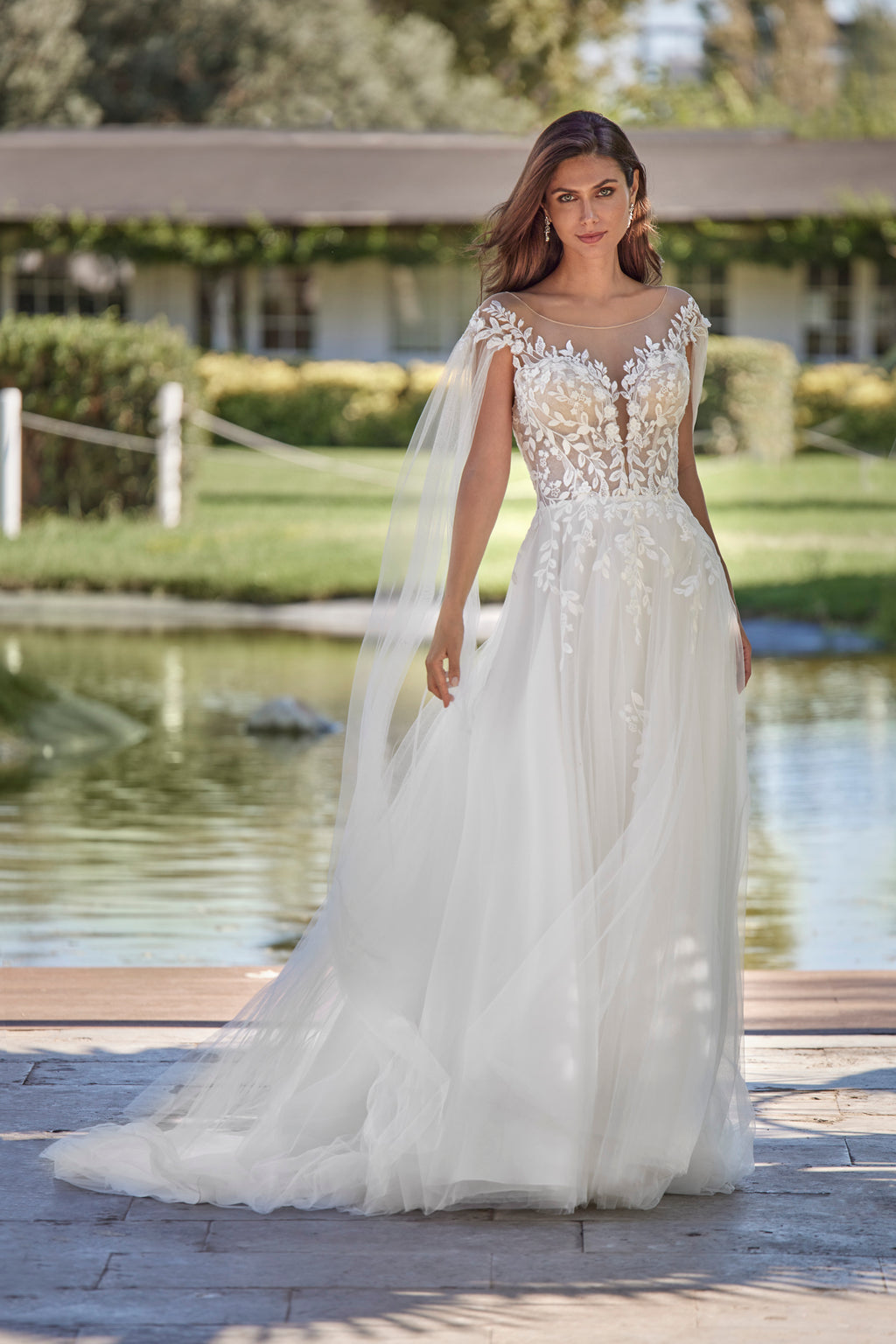 Woman in a white wedding dress standing outdoors by a body of water.