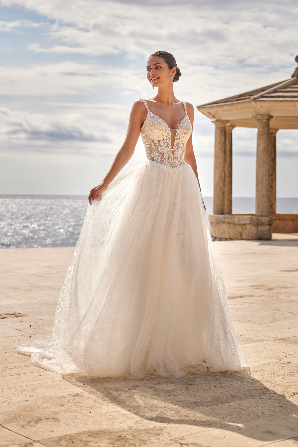 Woman in a white wedding dress standing on a beach with a gazebo in the background.