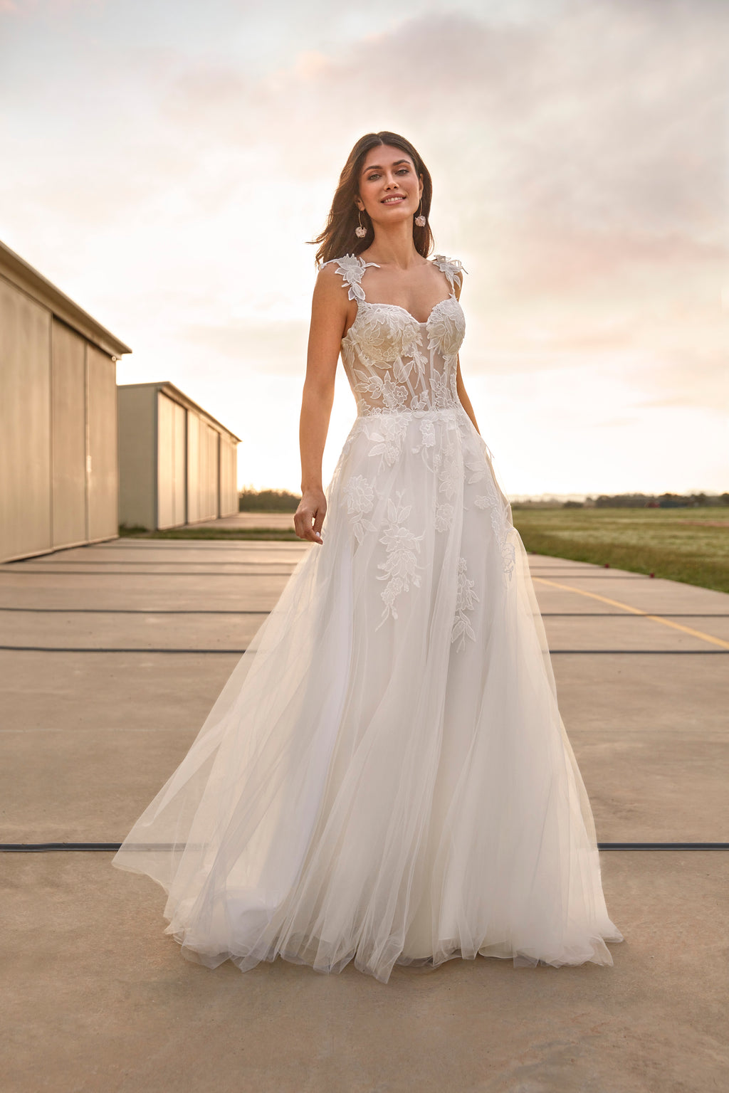 Woman in a white wedding dress standing on an airstrip with a cloudy sky.