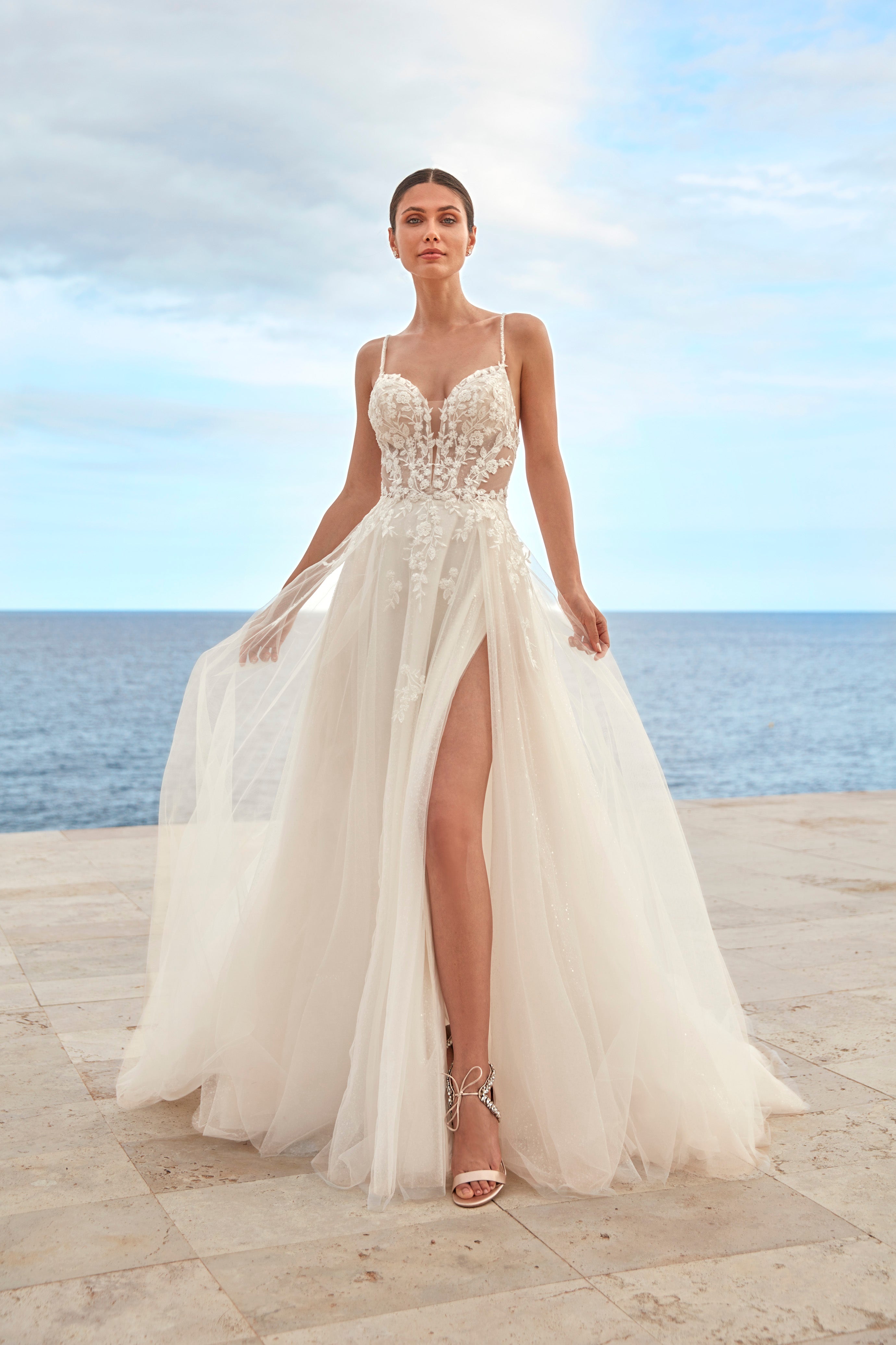 Woman in a white wedding dress standing on a beach with ocean view