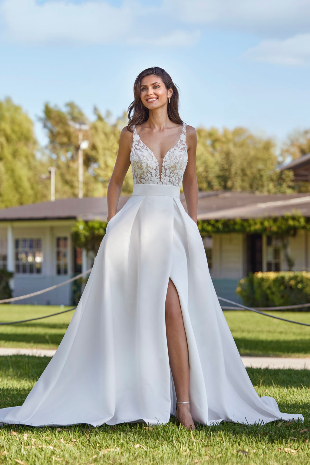 Woman in a white wedding dress with a high slit standing outdoors.