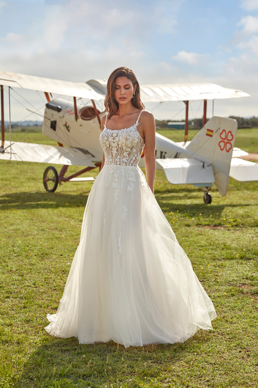 Woman in a white dress standing in front of an old airplane on a grassy field.