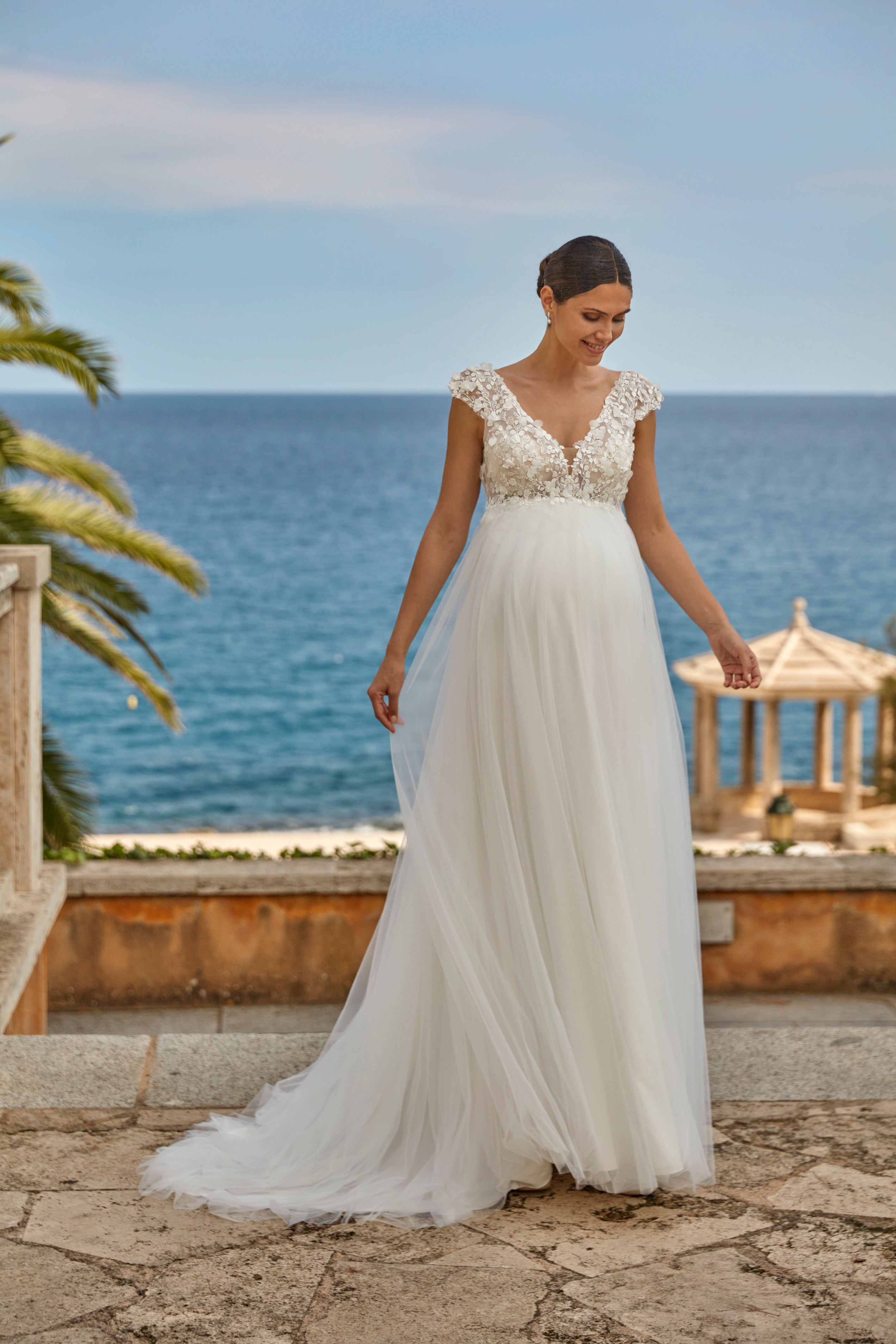 Woman in a white wedding dress standing by the ocean with a gazebo in the background.