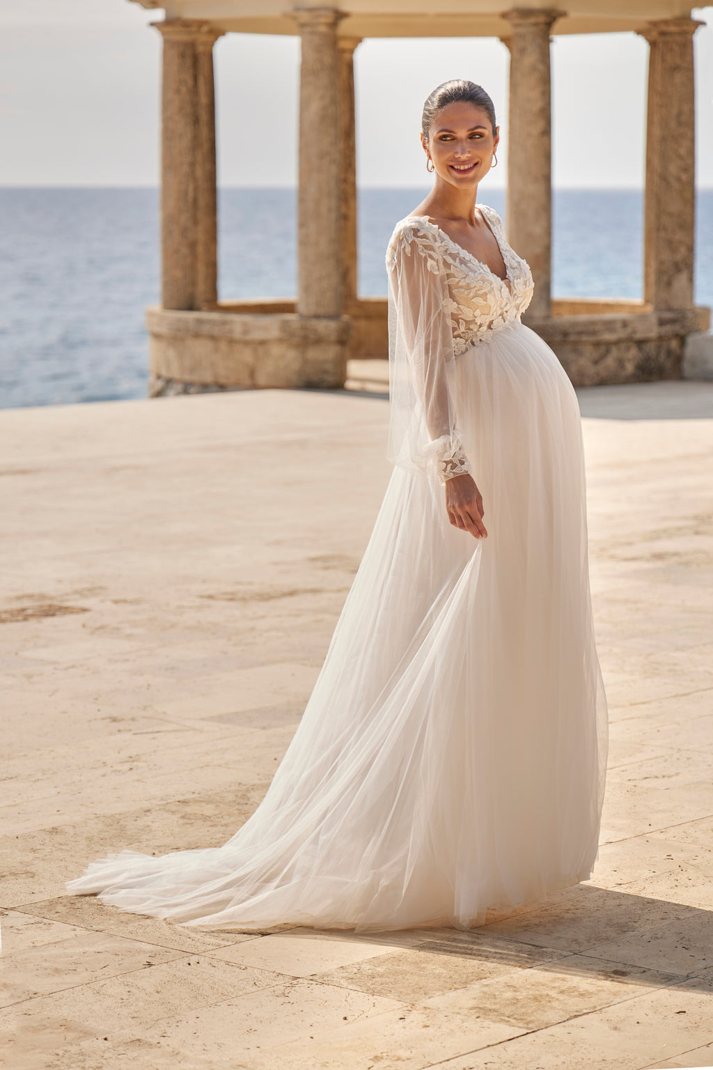 Woman in a white wedding dress standing in front of classical architecture with ocean view