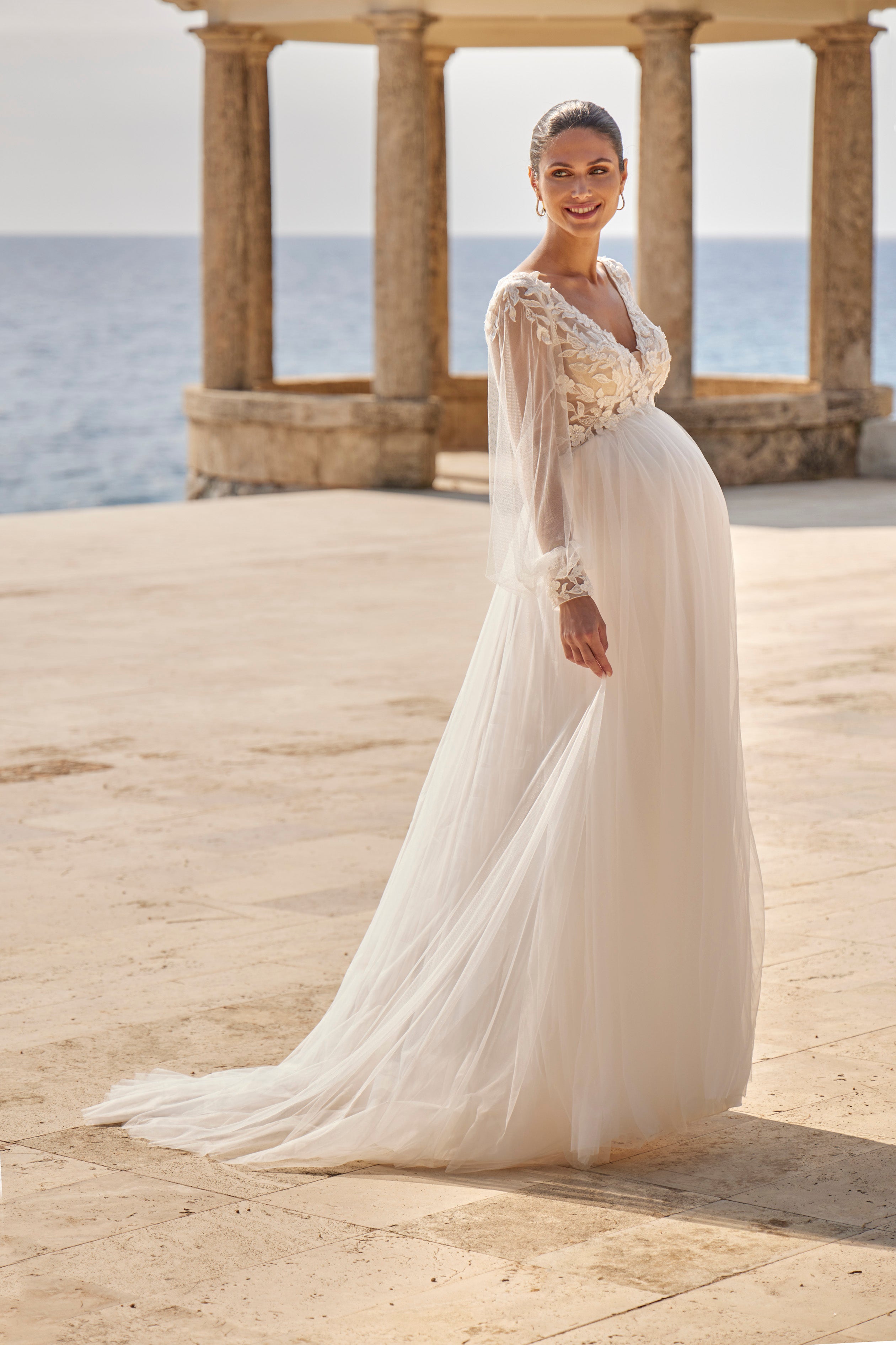 Woman in a white wedding dress standing in front of classical architecture with ocean view