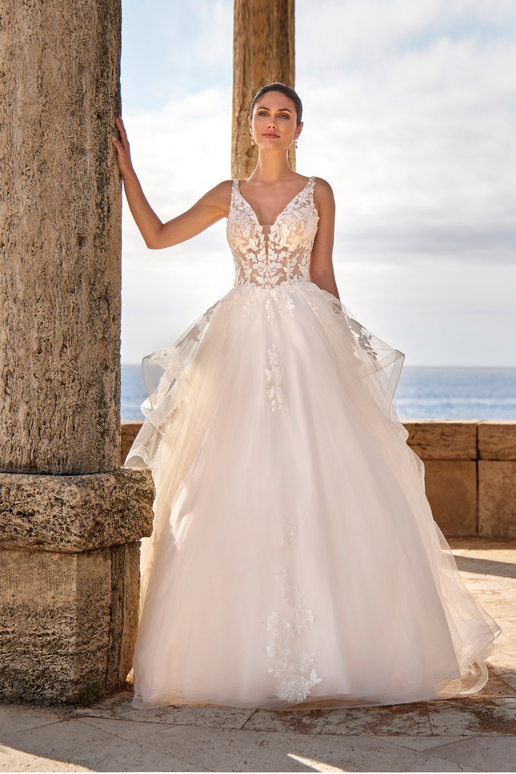 Woman in a white wedding dress standing next to stone columns with an ocean view.