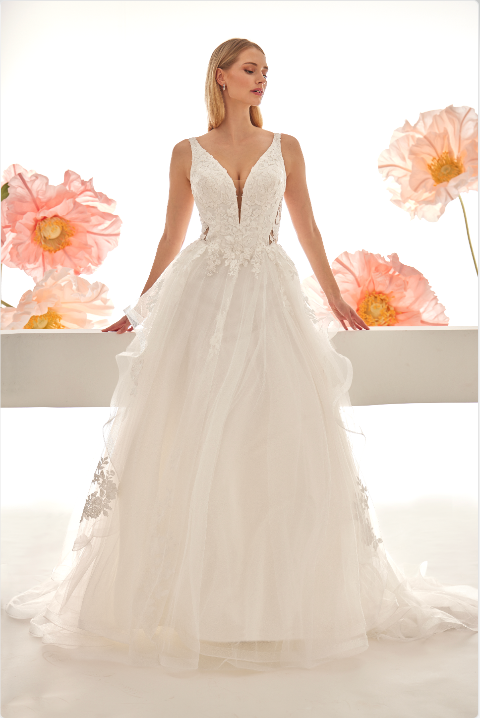 Woman wearing a white wedding dress with floral details against a white background with pink flowers.