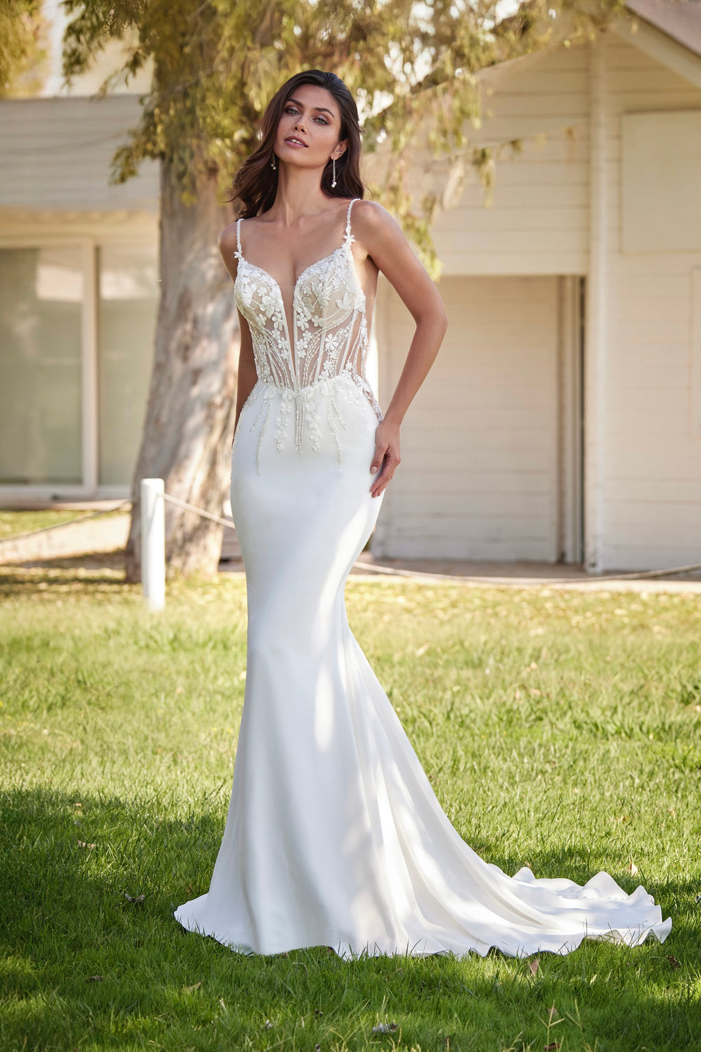 Woman in a white wedding dress standing outdoors on grass.