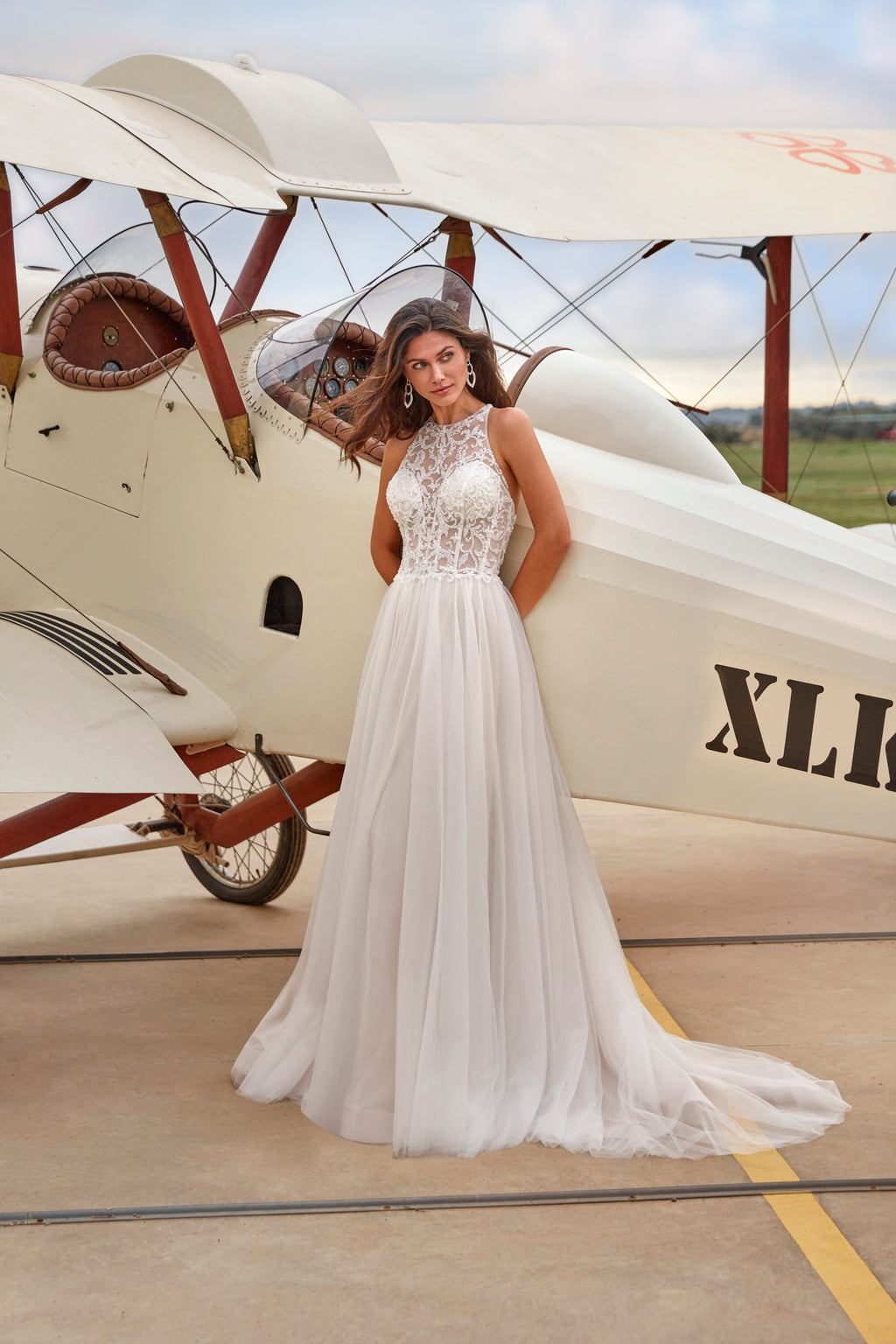 Woman in a white wedding dress standing in front of an old biplane on an airfield.