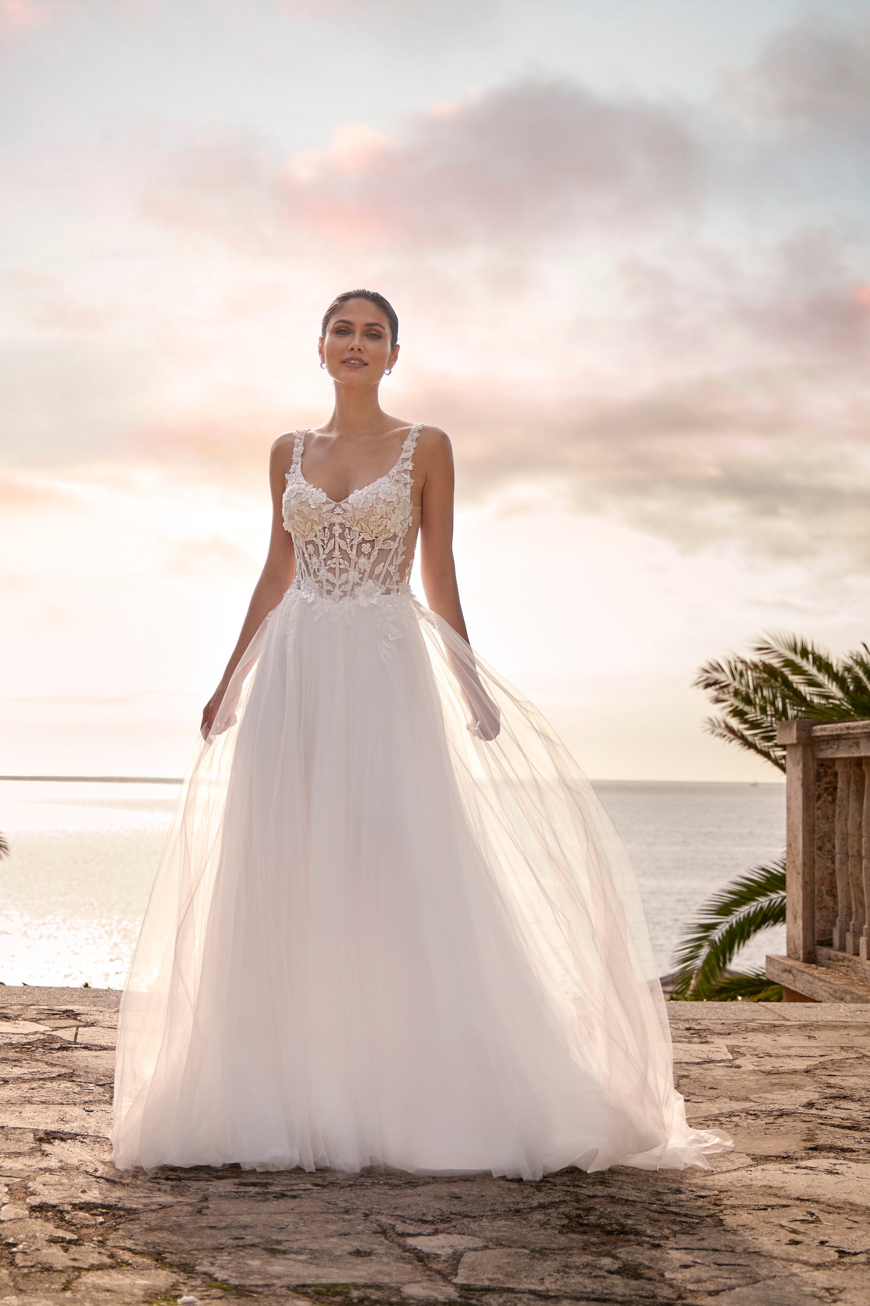 Woman in a white wedding dress standing on a beach with a sunset in the background