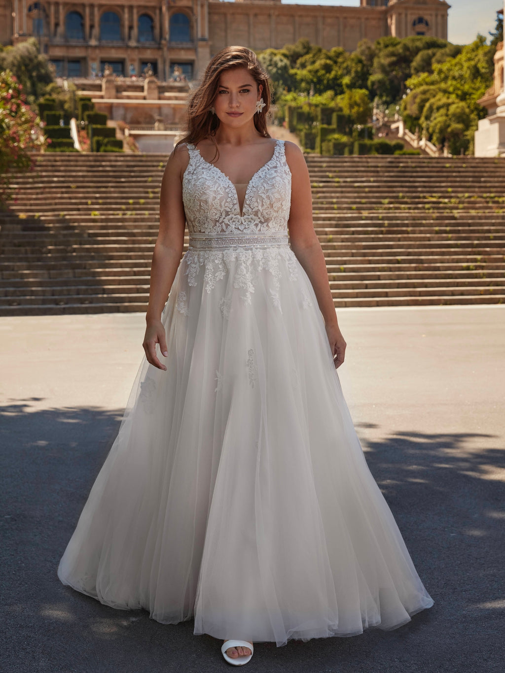 Woman in a white wedding dress standing in front of a historical building with steps and greenery.