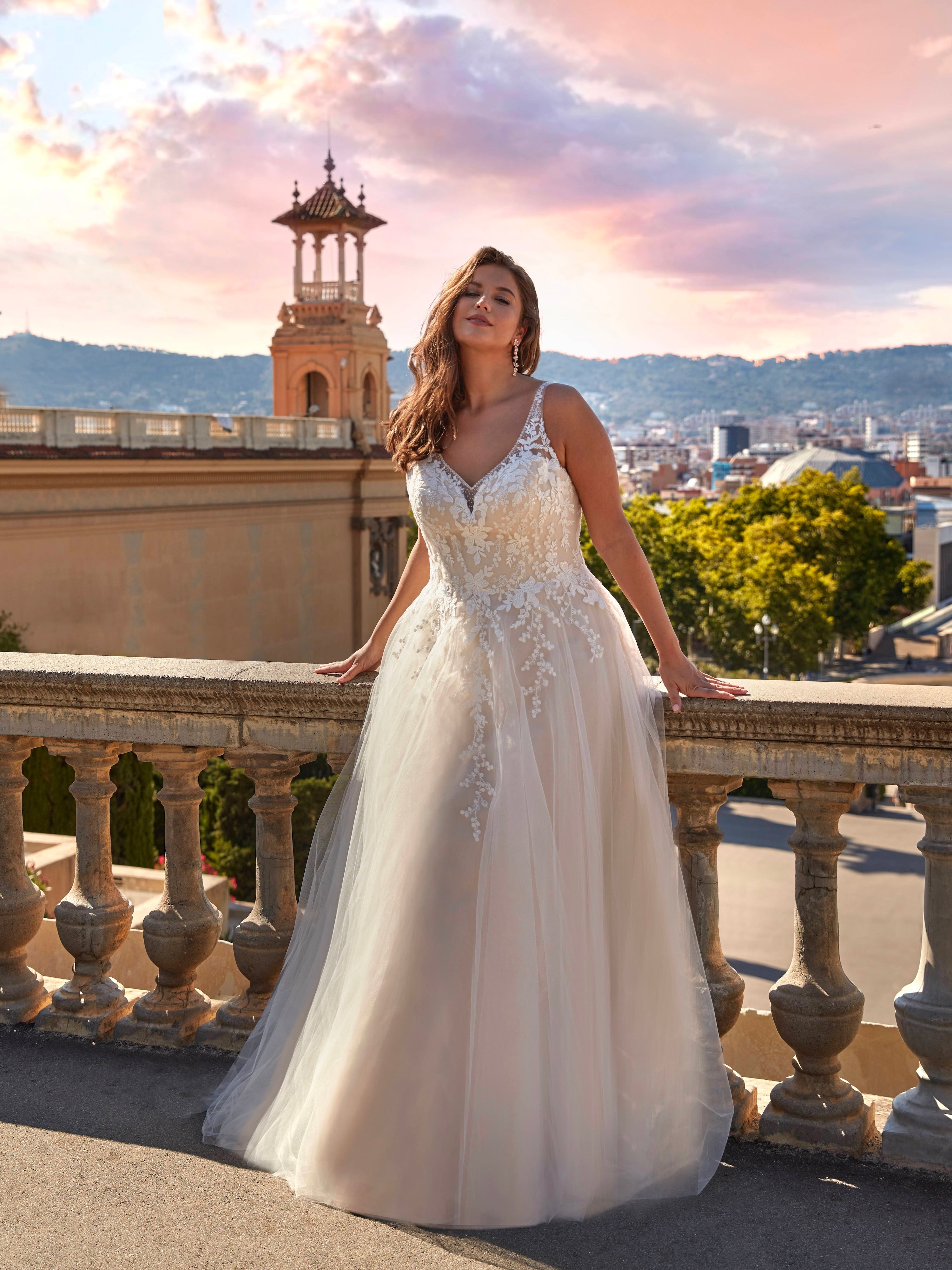 Woman in a white wedding dress standing on a balcony with a cityscape in the background