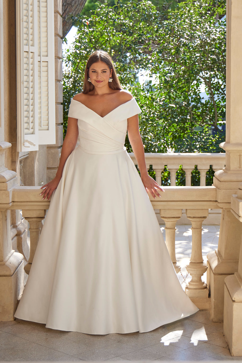 Woman in a white wedding dress standing on a balcony with greenery in the background