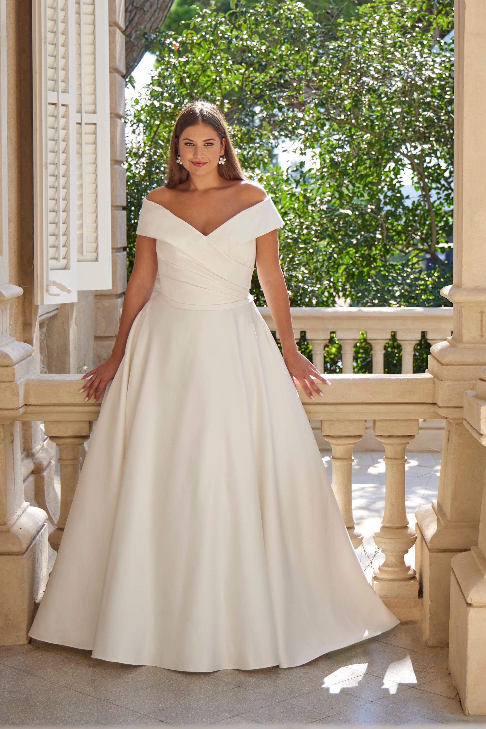 Woman in a white wedding dress standing on a balcony with greenery in the background